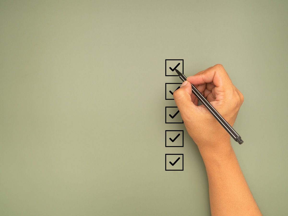 Hand holding a pen check-marking on the checklist box on a green background