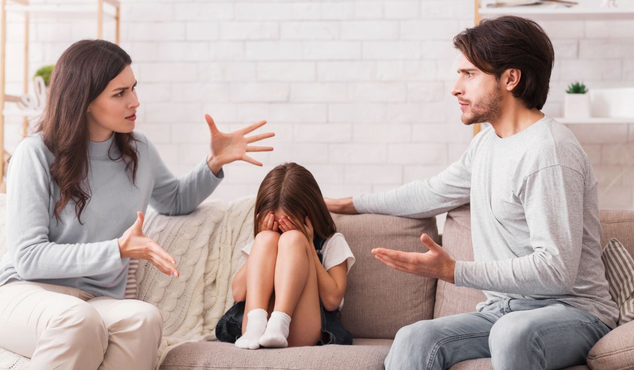 Crying little girl sitting between arguing parents on sofa