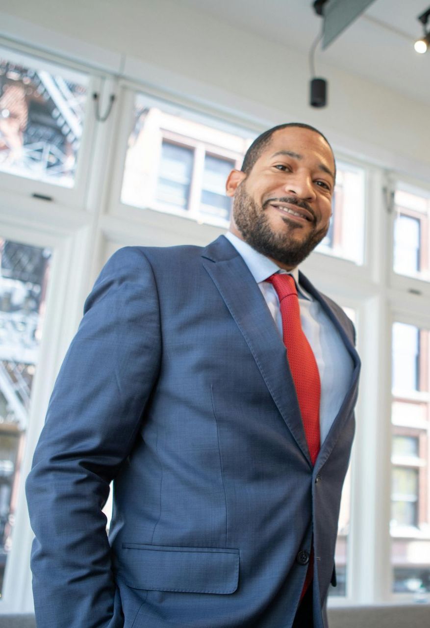 A man in a suit and tie is standing in front of a window.