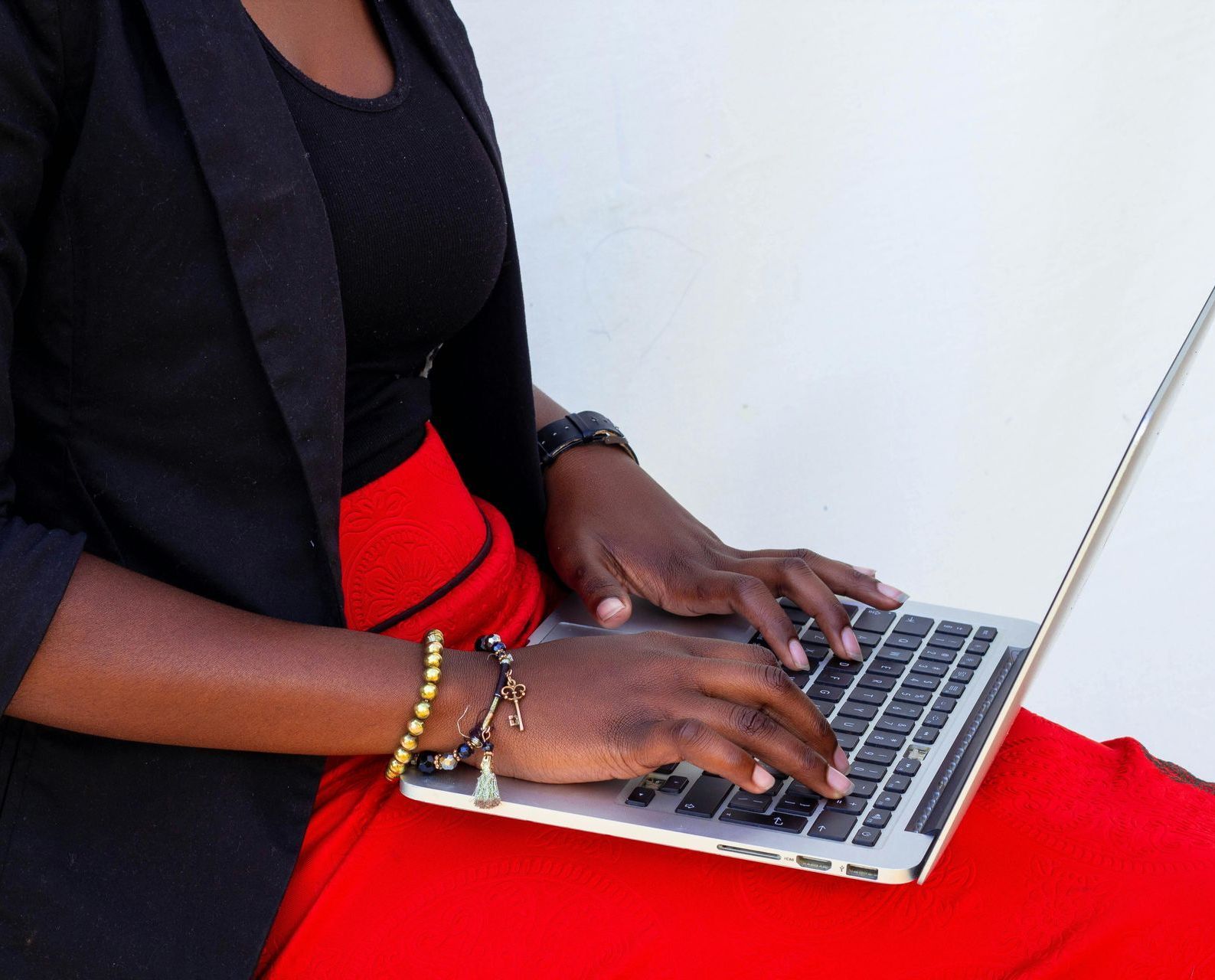 A woman in a red skirt is typing on a laptop computer.