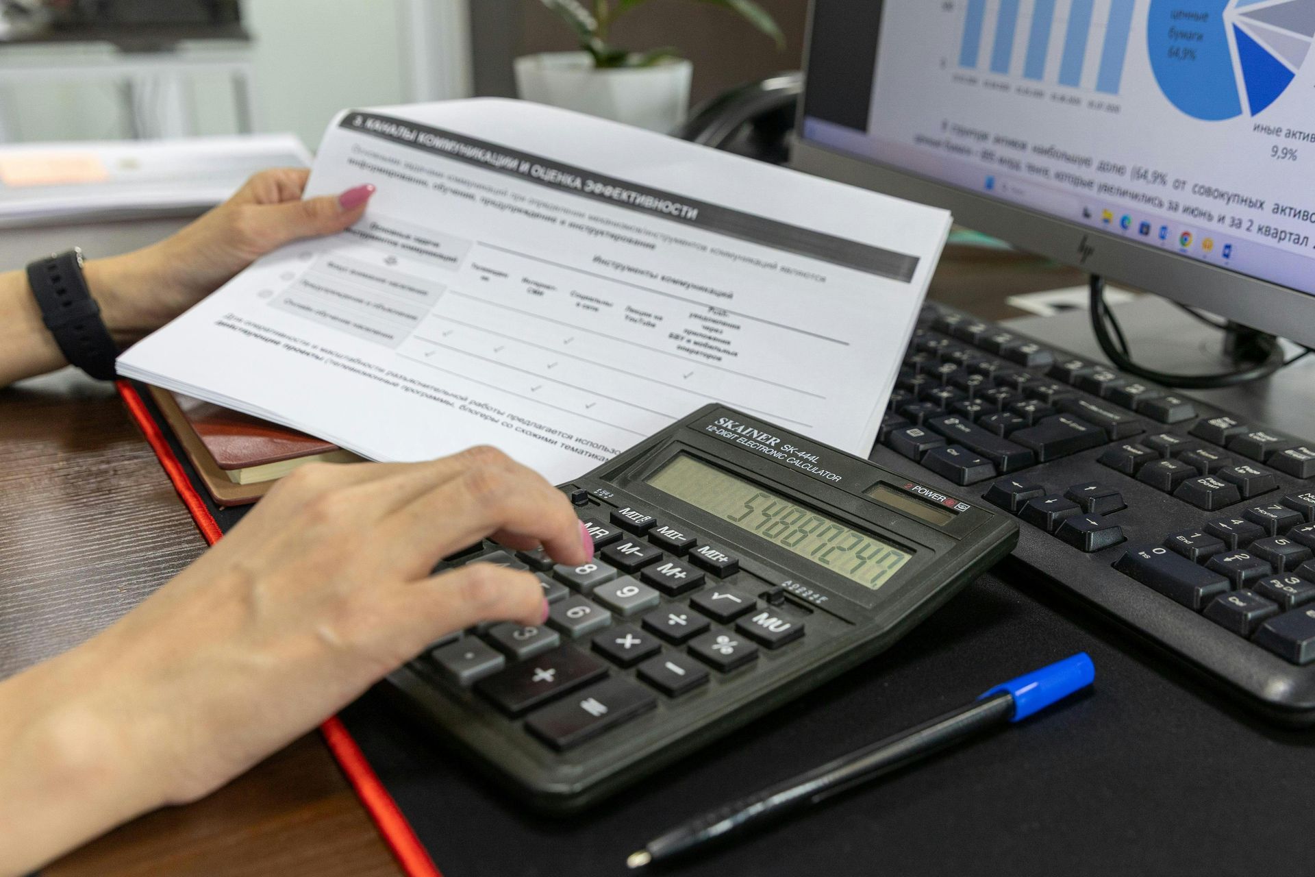 A person is typing on a calculator while holding a piece of paper.