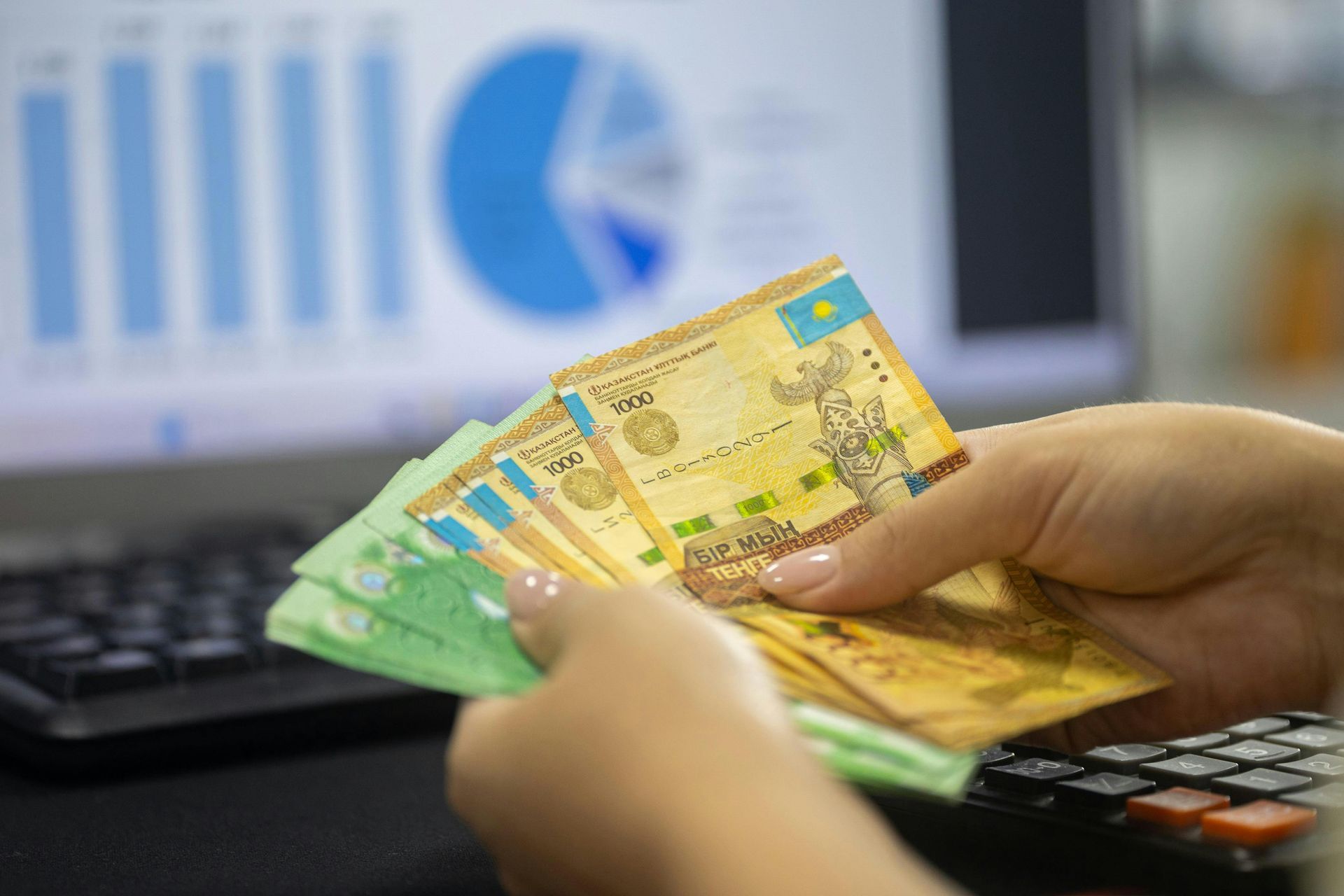 A person is holding a bunch of money in front of a laptop computer.