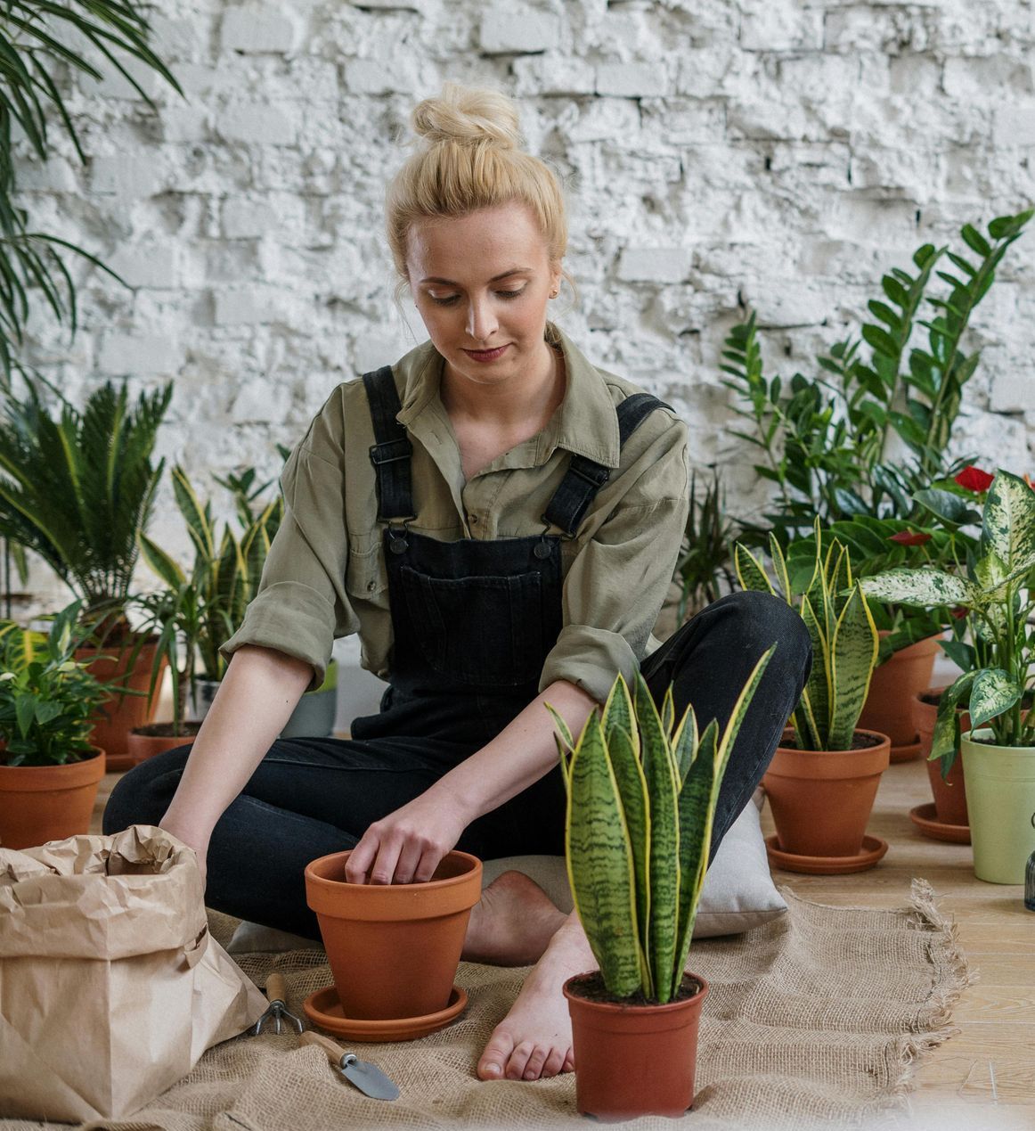A woman is sitting on the floor surrounded by potted plants.