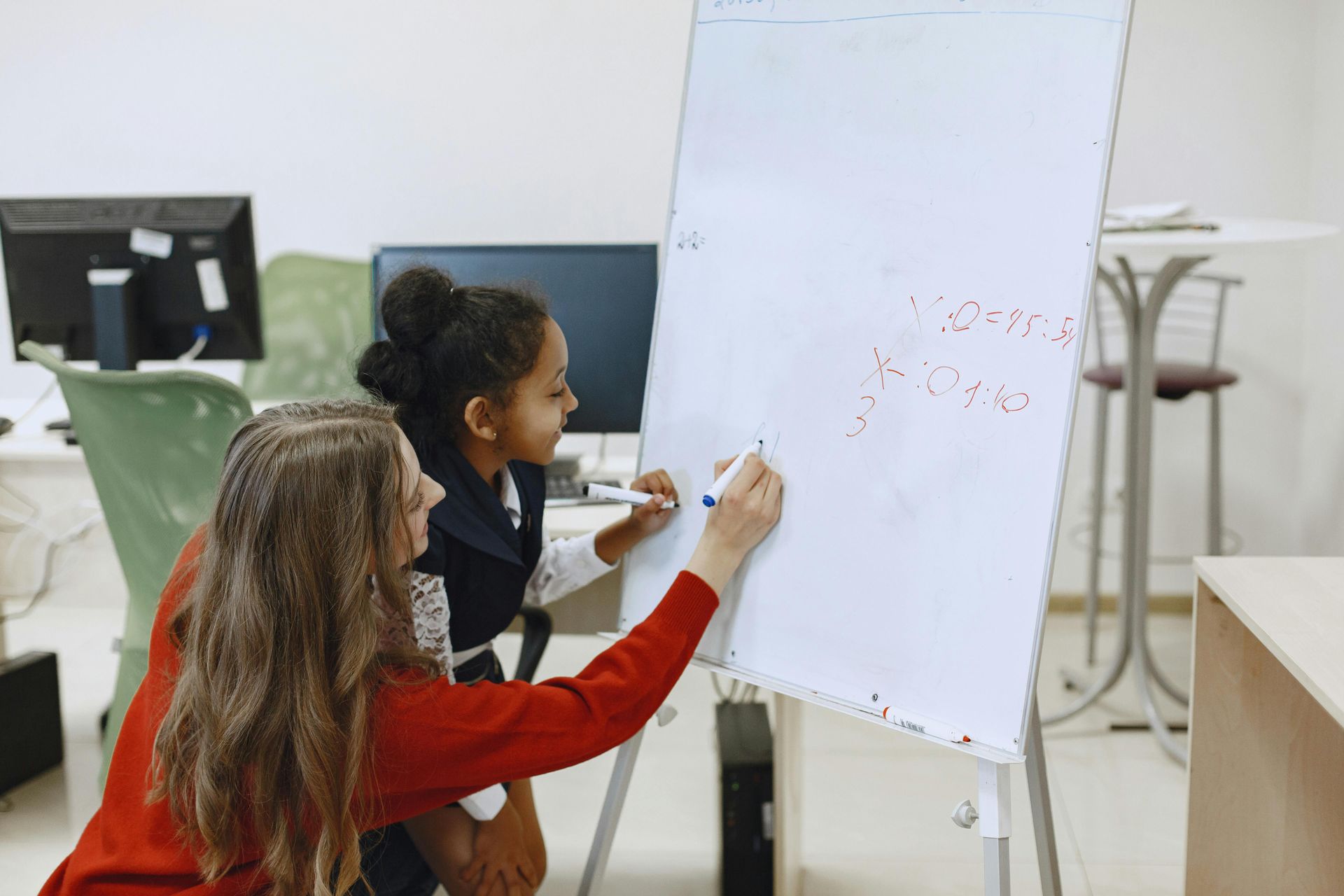 A woman is teaching a young girl how to write on a whiteboard.