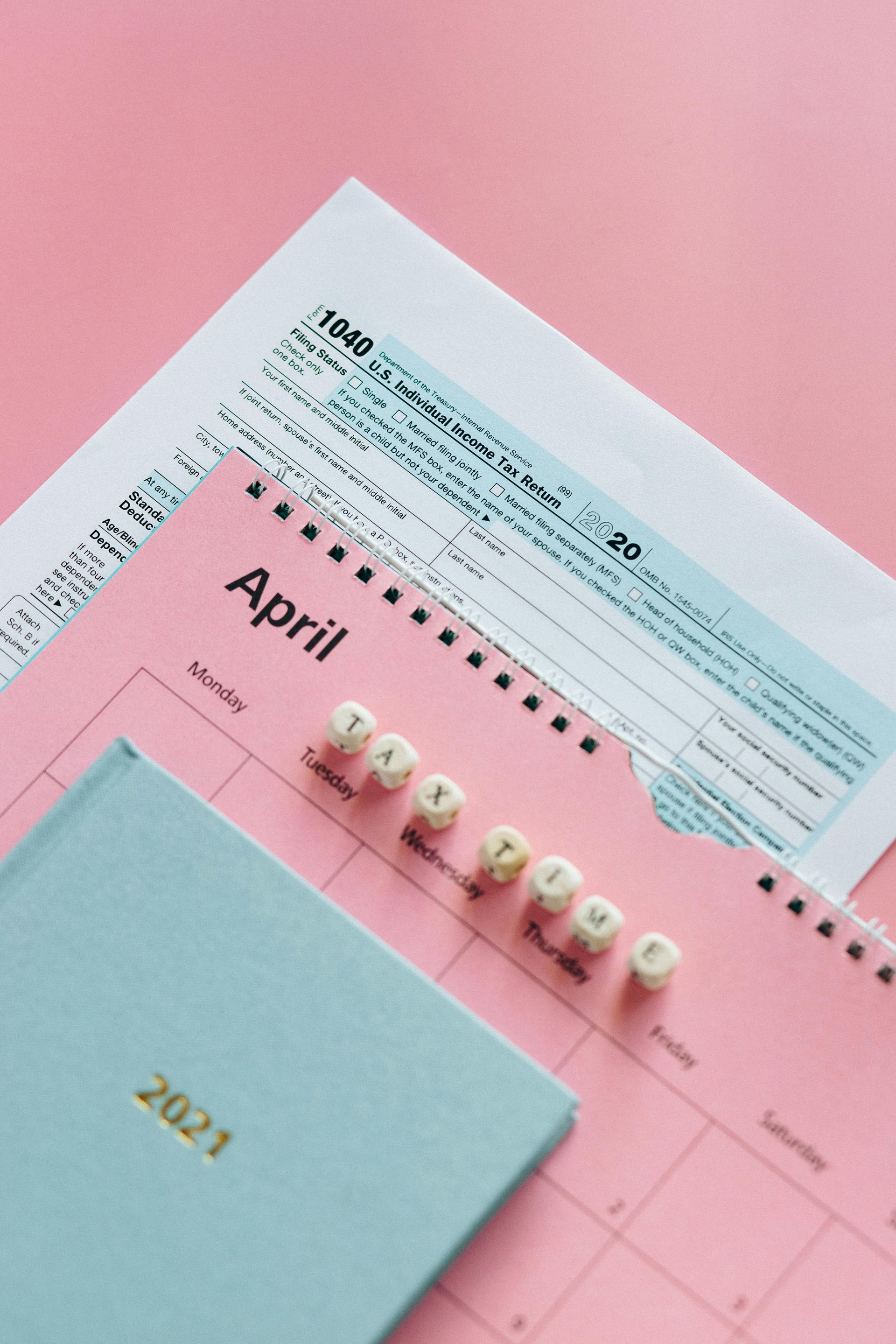 A calendar and a tax form are on a pink table.