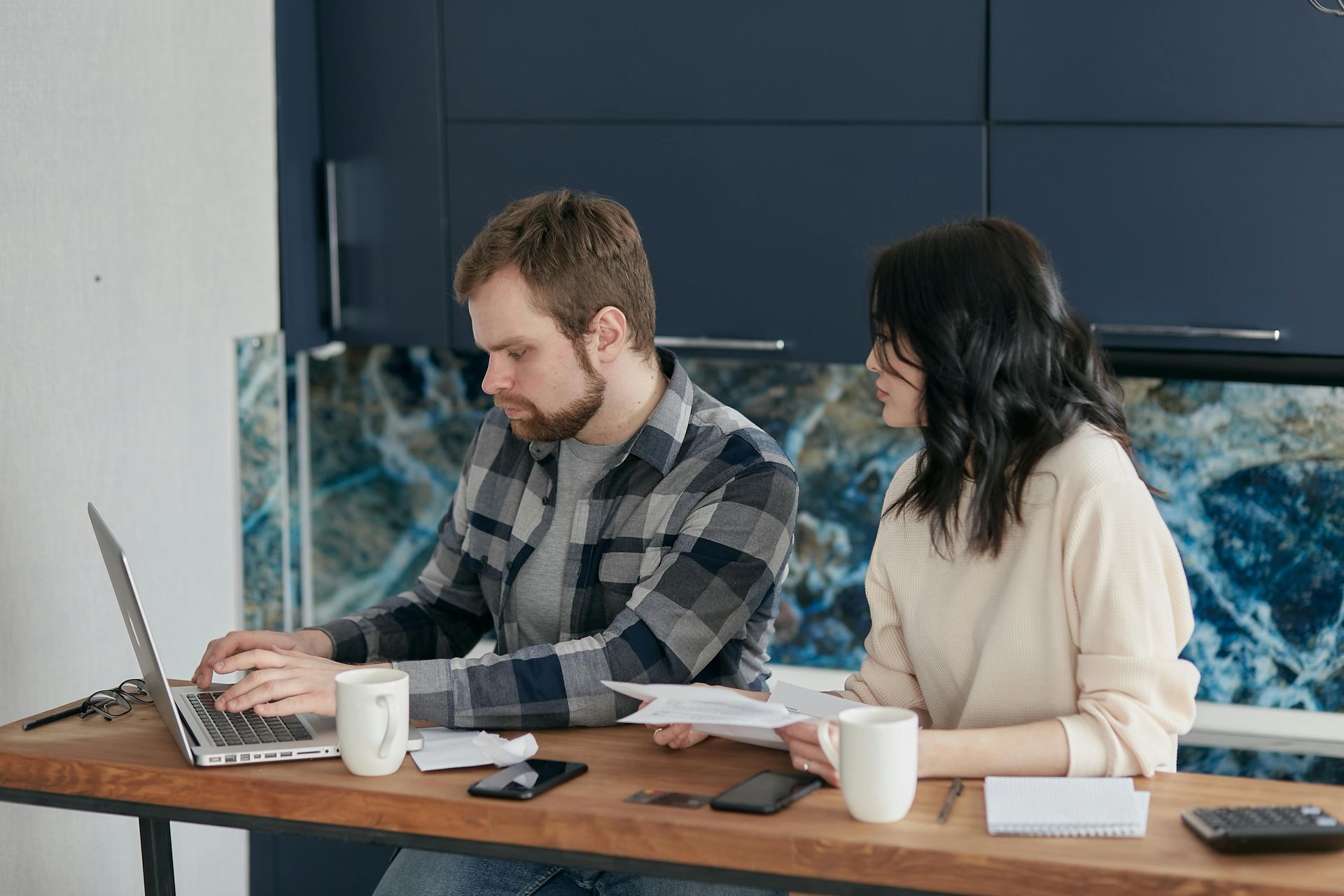 A man and woman sitting at a table looking over a laptop with financial information