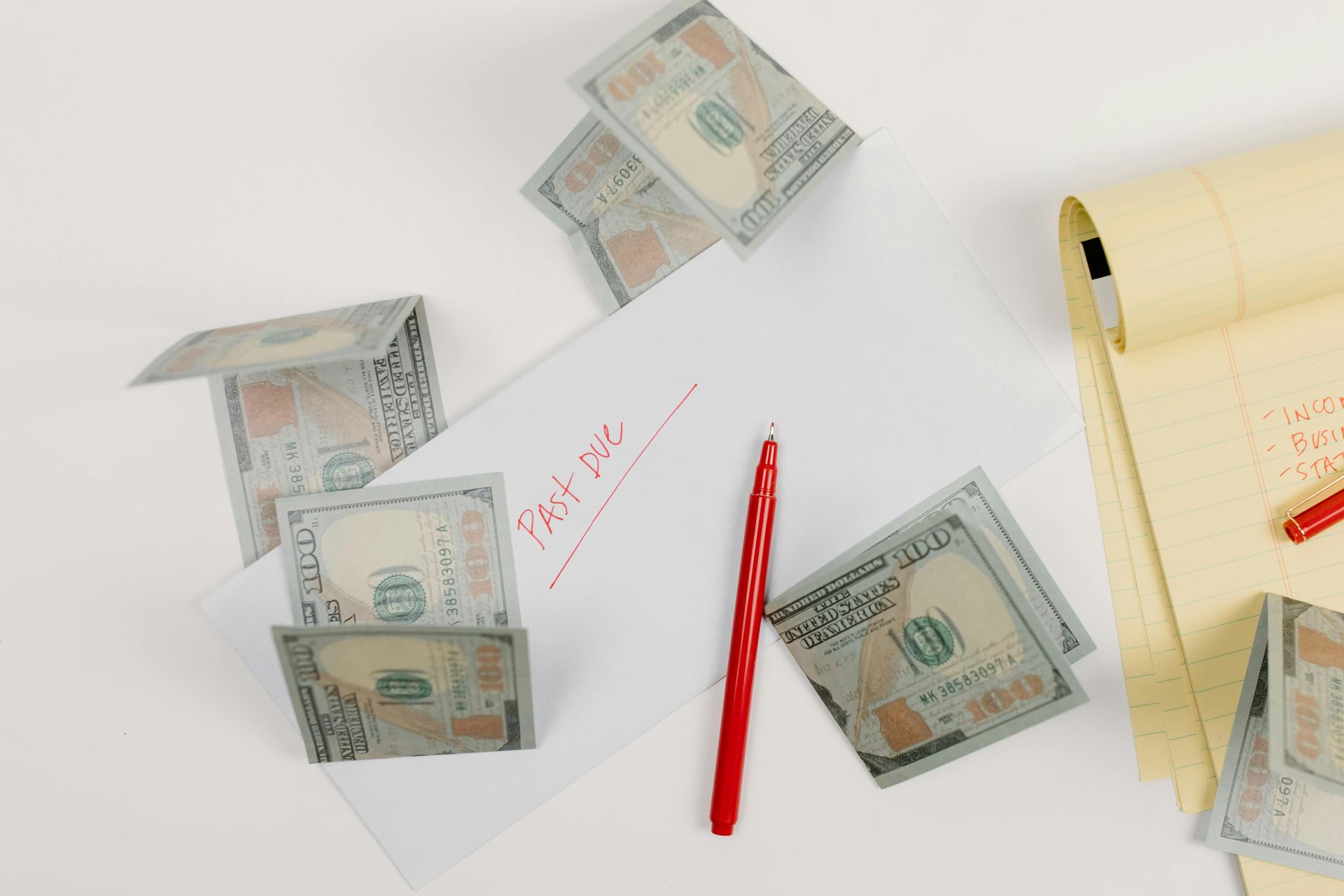 A bunch of money is falling on a piece of paper with a pen.