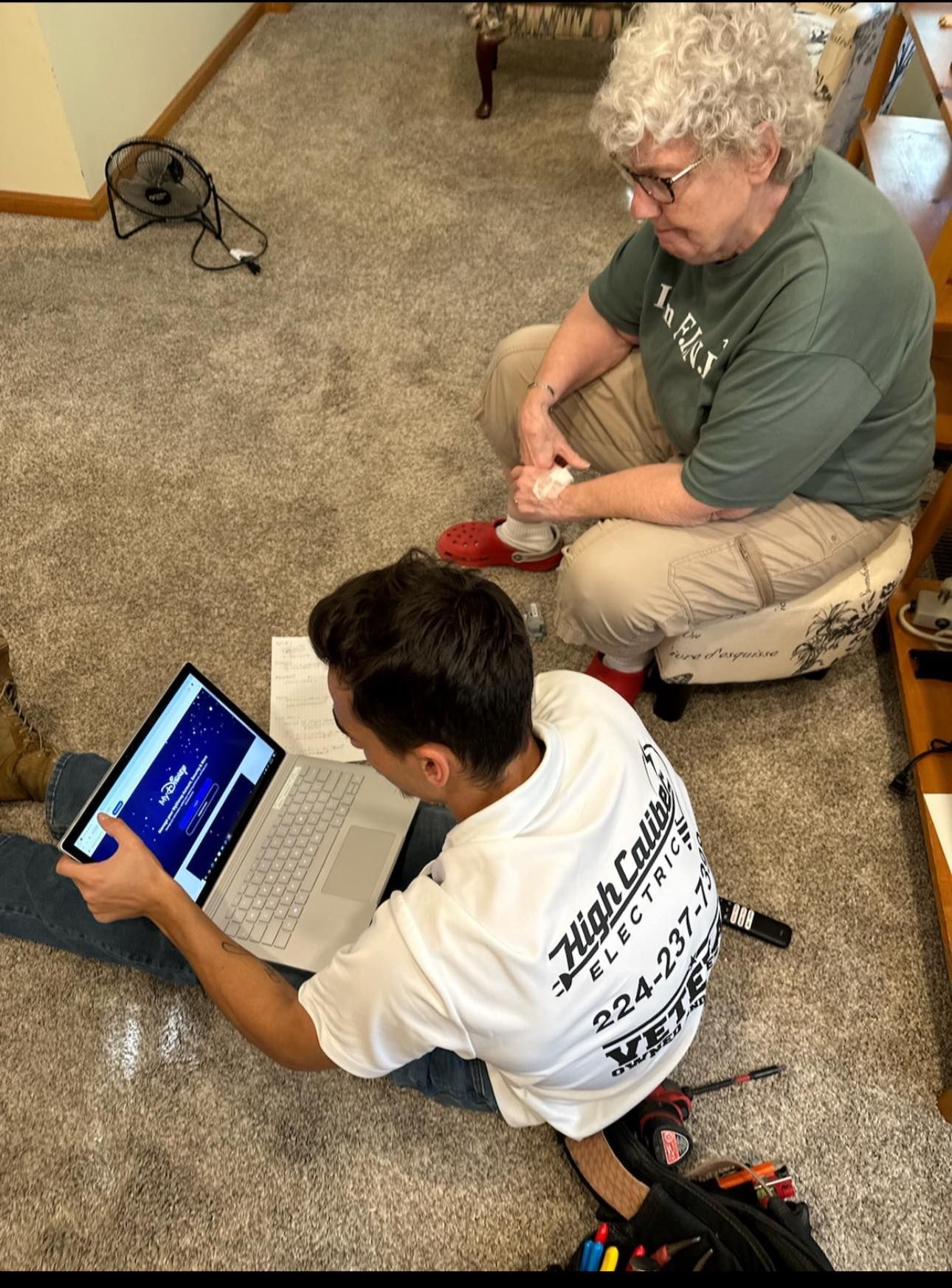 A man and a woman are sitting on the floor looking at a laptop.