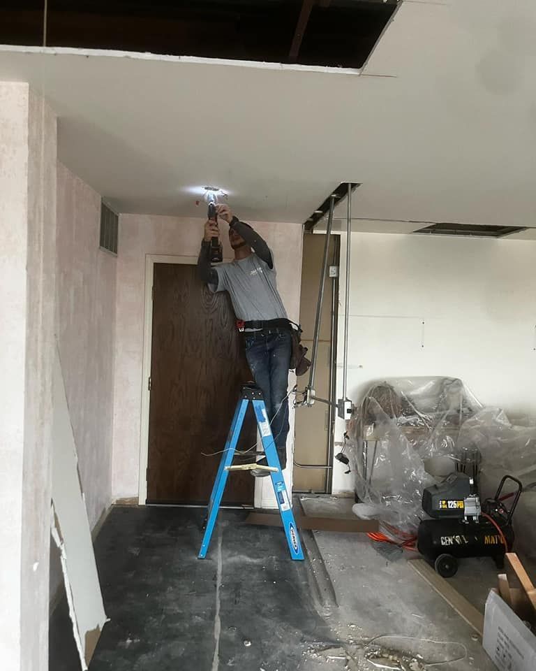 A man is standing on a ladder working on a light fixture.