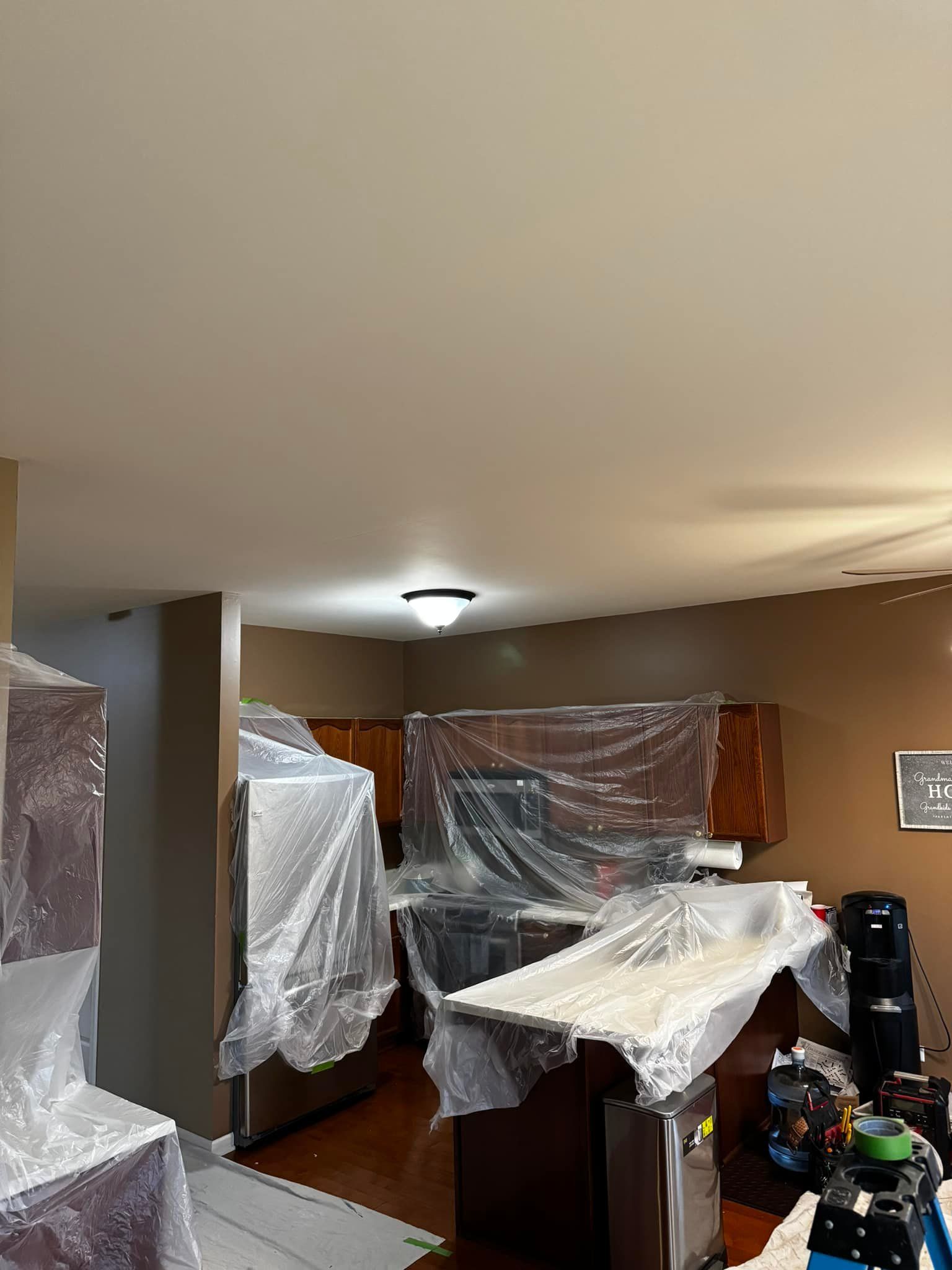 A kitchen is being painted and covered in plastic wrap.