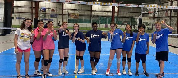 A group of young people are posing for a picture on a volleyball court.