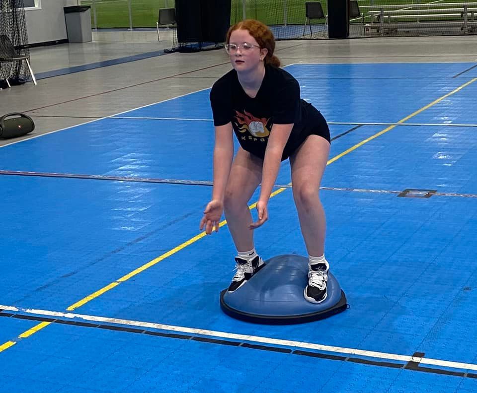 A young girl is standing on a balance ball on a basketball court.