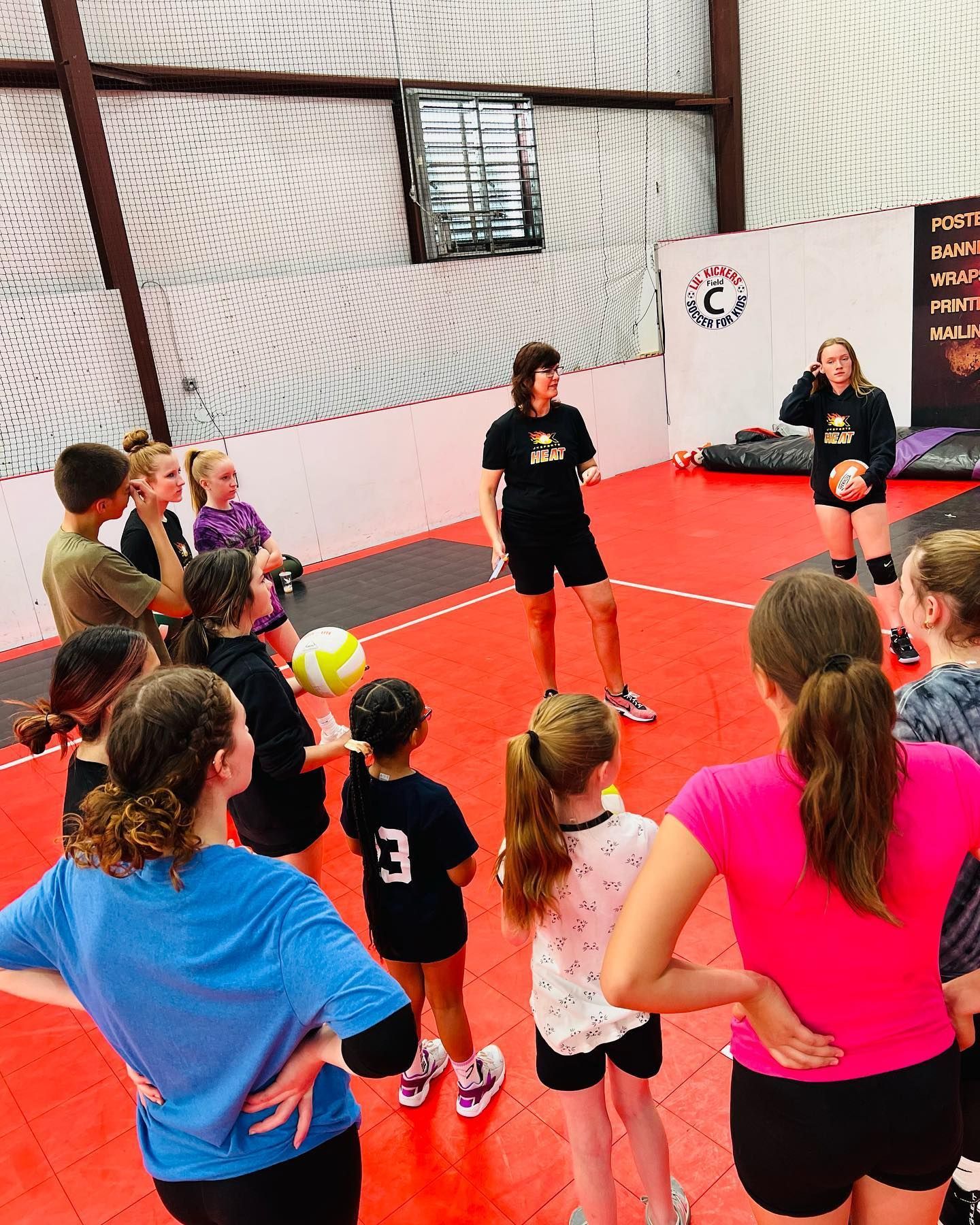 A group of young girls are standing in a circle on a volleyball court.
