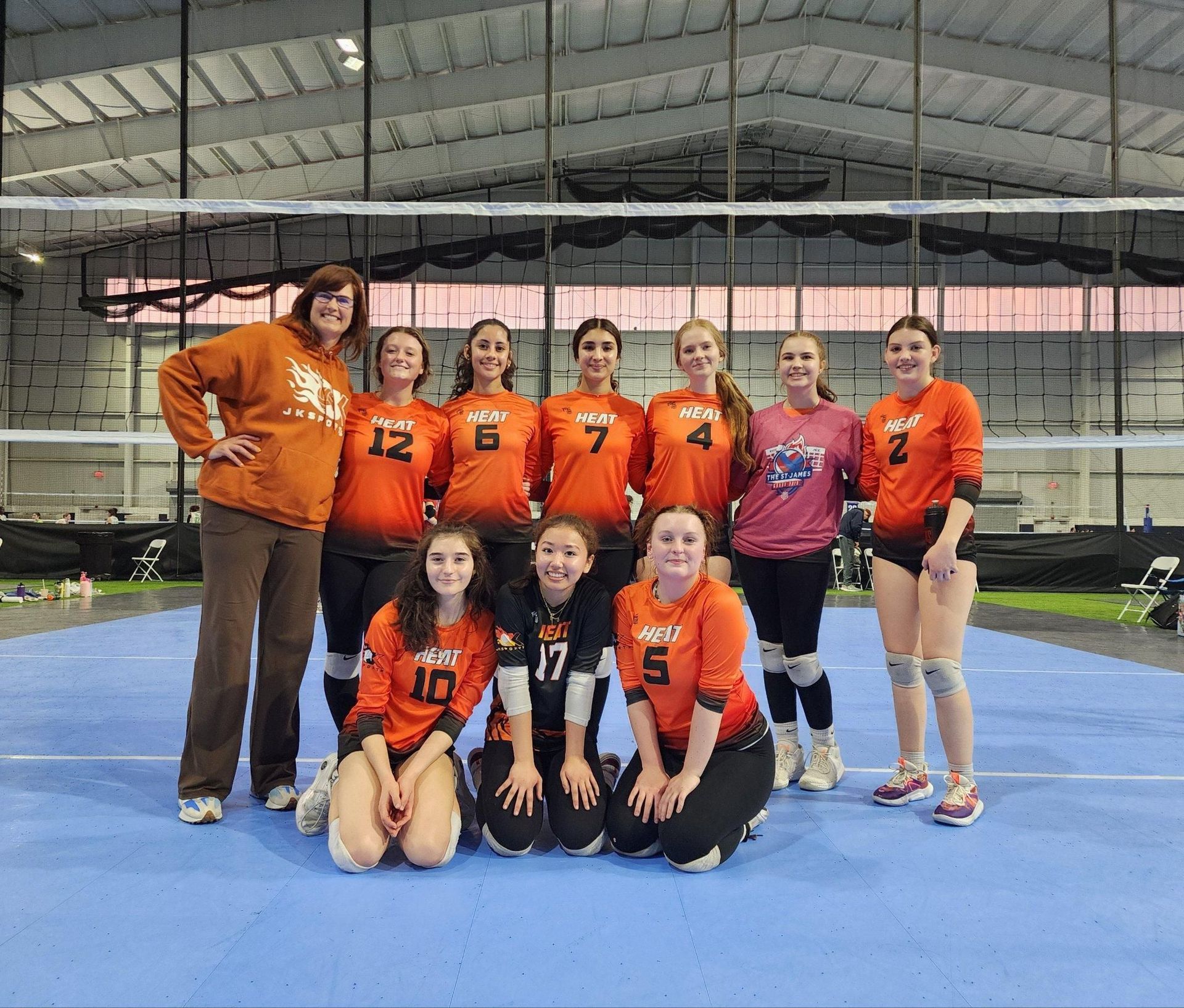 A group of girls are posing for a picture on a volleyball court.