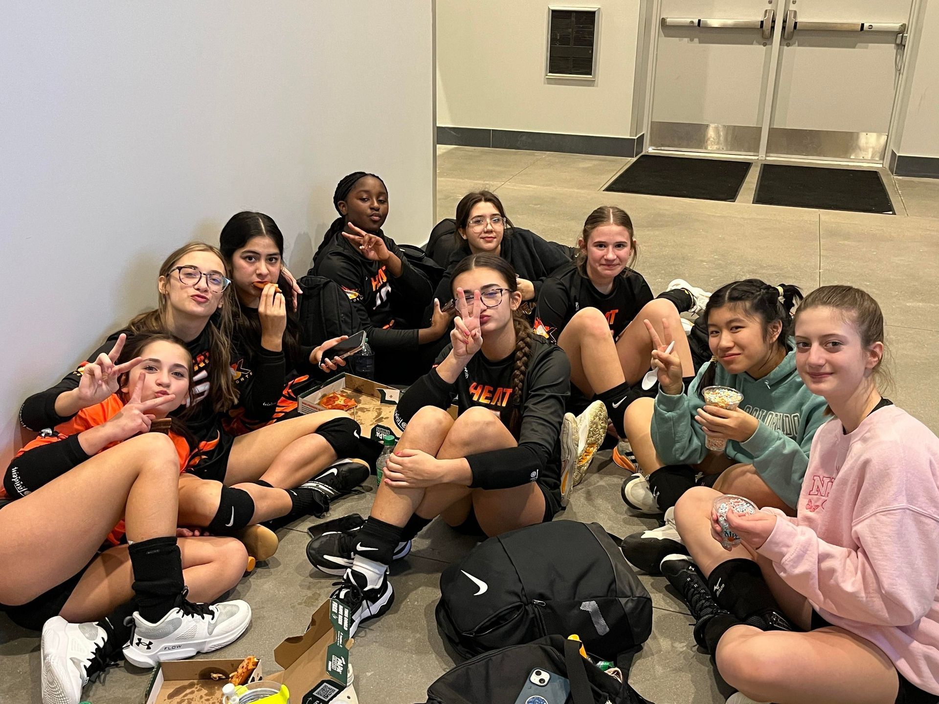 A group of young girls are sitting on the floor eating pizza.