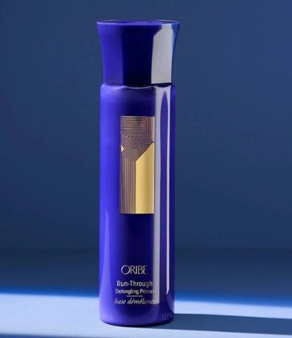 Tall dark blue bottle with shiny gold zigzag logo and Oribe Run-Through Detangling Primer printed at bottom.