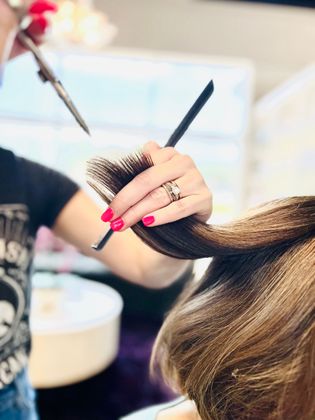 Haircut showing stylist holding section of client's hair between fingers & scissors poised to cut the strands.