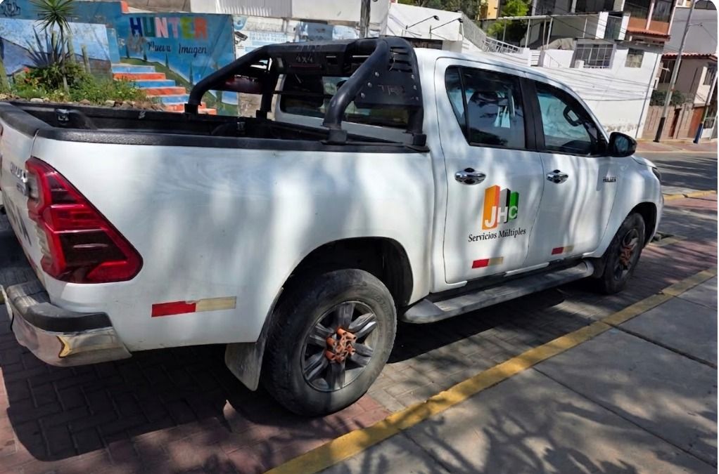 Una camioneta blanca estacionada en una acera, en una calle, con el logotipo municipal en la puerta del pasajero.