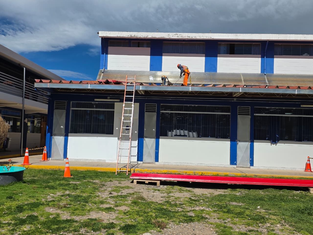 Un obrero de la construcción, vestido con ropa de trabajo naranja, trabaja en el tejado de un edificio azul y blanco