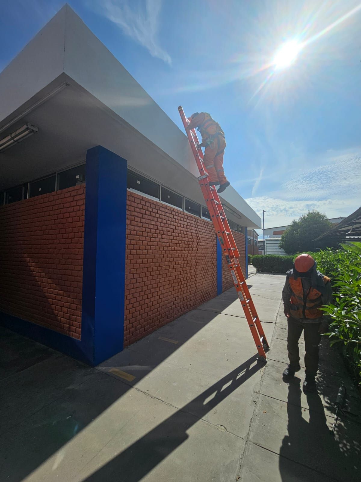 Un trabajador con ropa de alta visibilidad sube por una escalera naranja adosada a un edificio con una pared naranja 