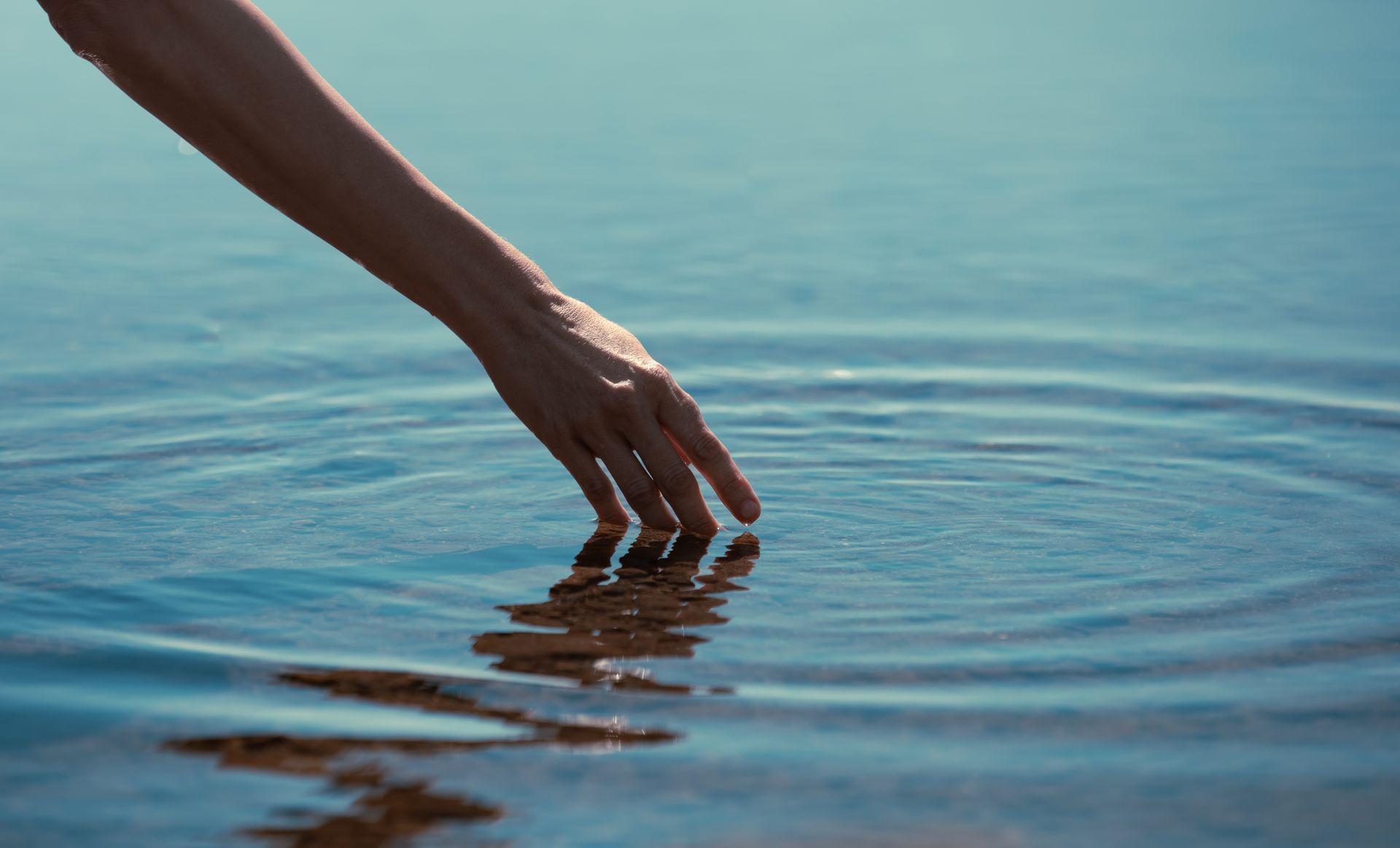 A woman 's hand is reaching into the water to touch it.