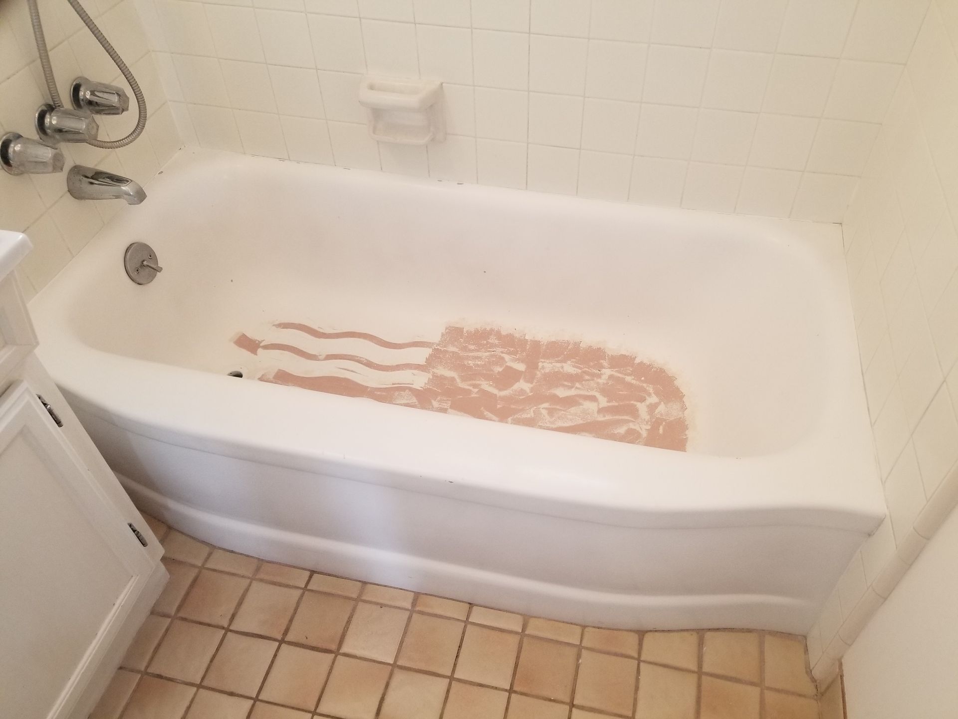 Bathtub filled with pinkish water, likely soapy, in a bathroom with tile floor and walls.