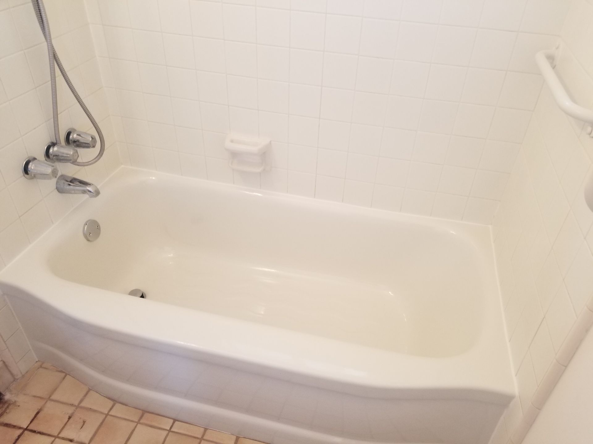 White bathtub with showerhead, faucet, and soap dish in a tiled bathroom.