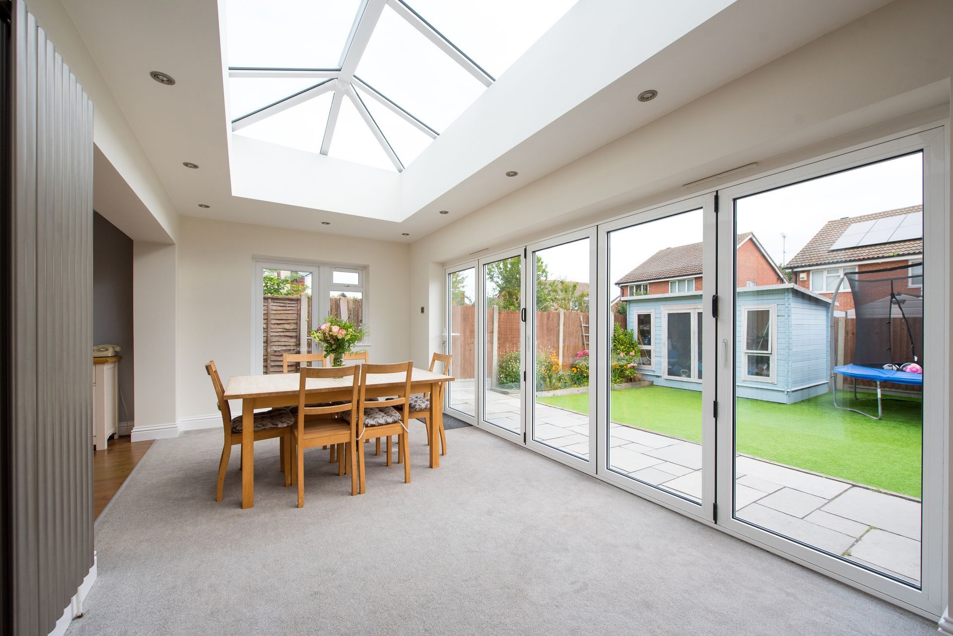 Dining room with skylight, large windows, dining table, chairs, and a view of the yard.