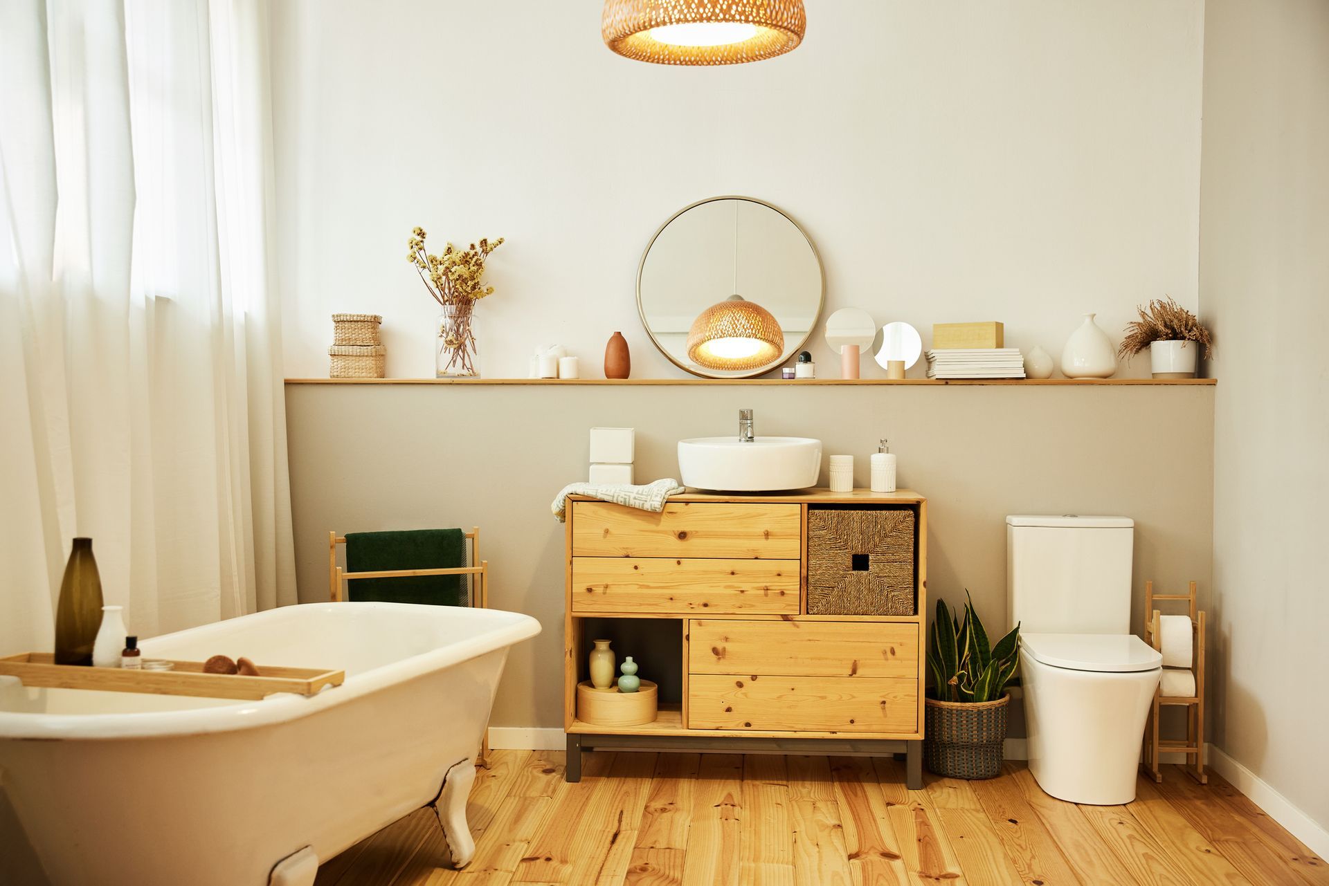 Bathroom with wooden vanity, white tub, and round mirror. Natural light and neutral tones create a serene space.
