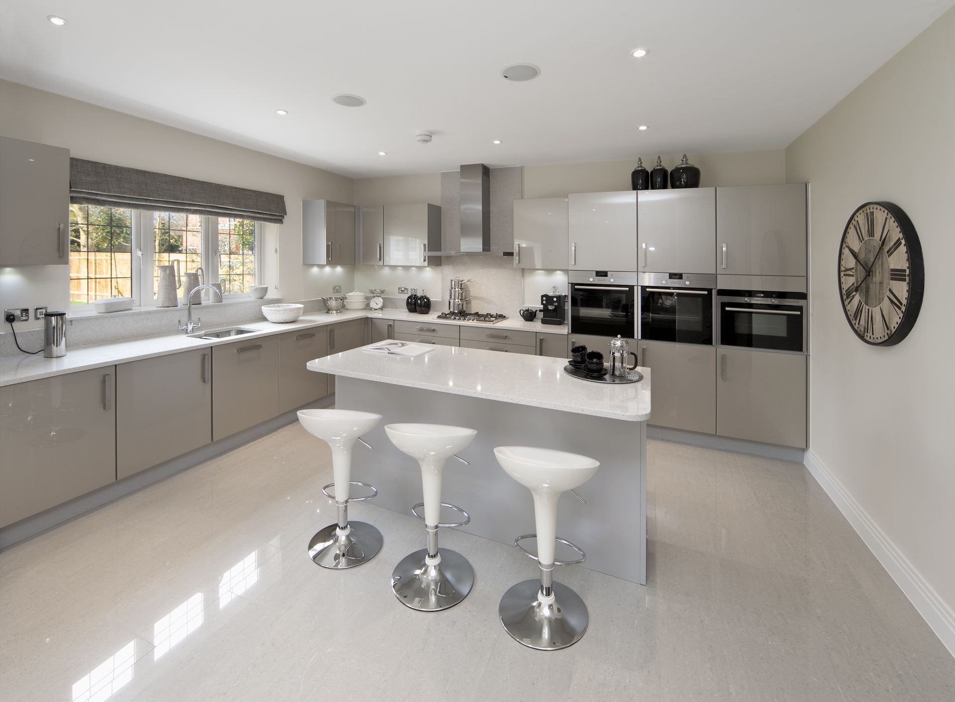Modern, light gray kitchen with island, three bar stools, and stainless steel appliances.
