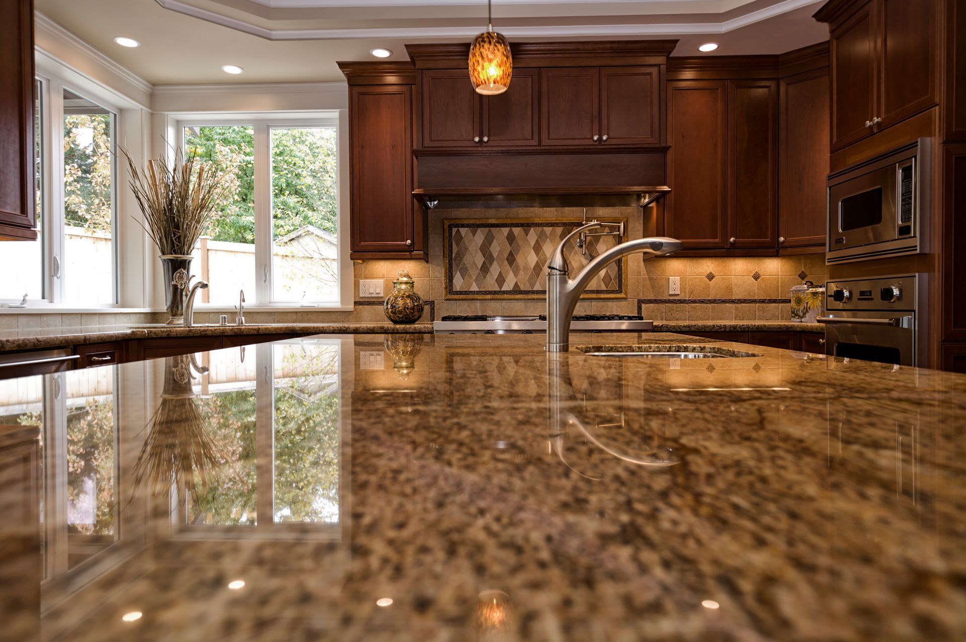 Granite countertop in a kitchen with dark wood cabinets, a window, and overhead lighting.