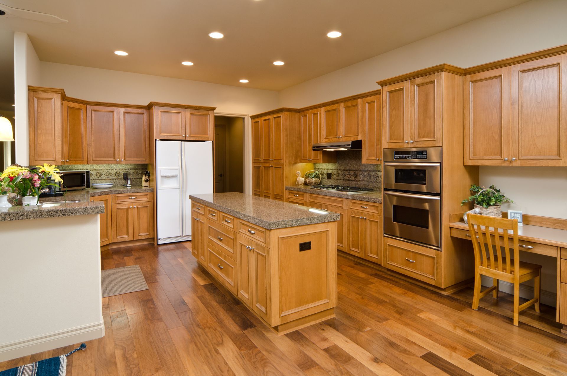 A light-wood kitchen with a large island, stainless steel appliances, and a desk.