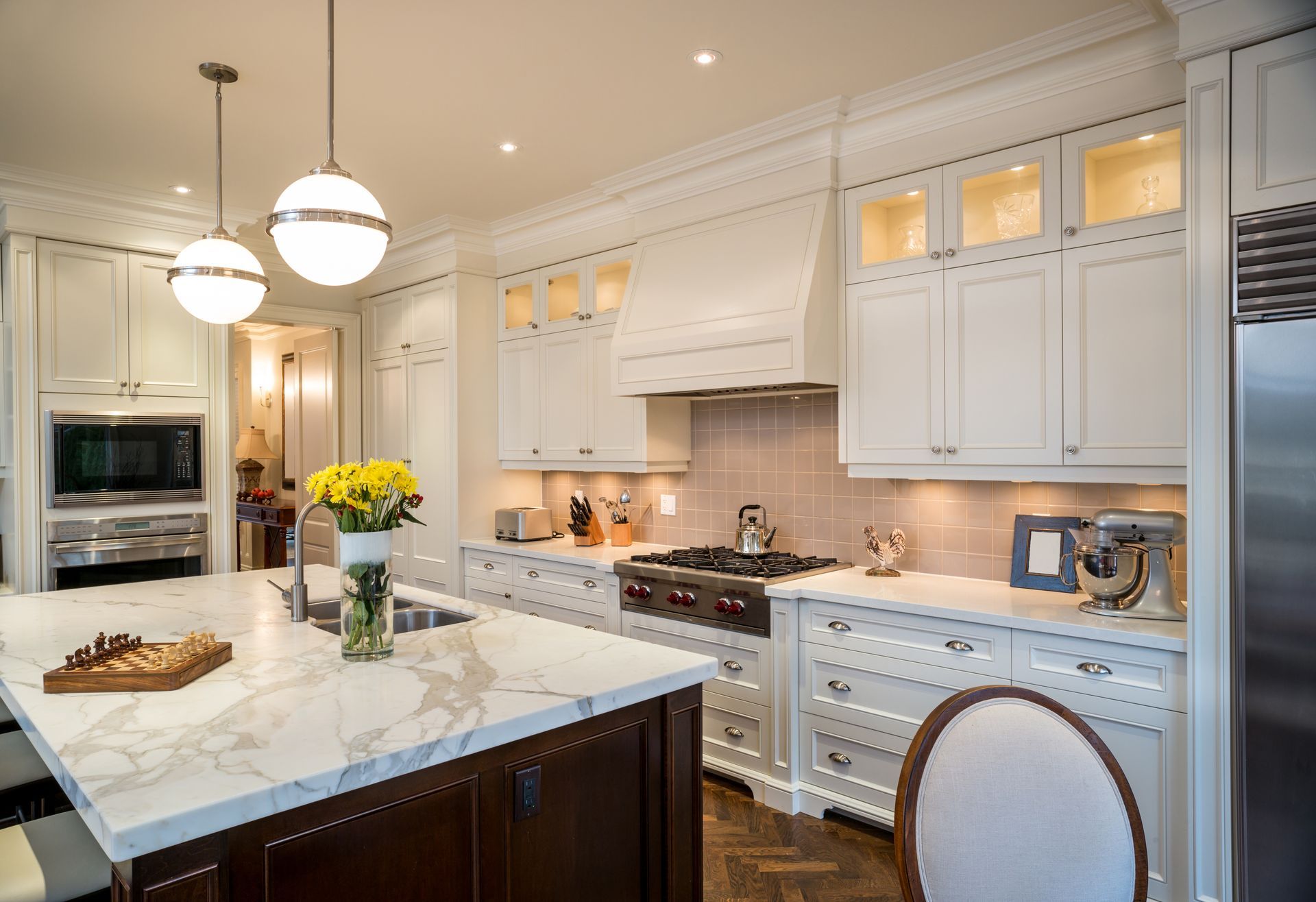 Elegant white kitchen with marble island, dark cabinets, stainless steel appliances, and pendant lighting.