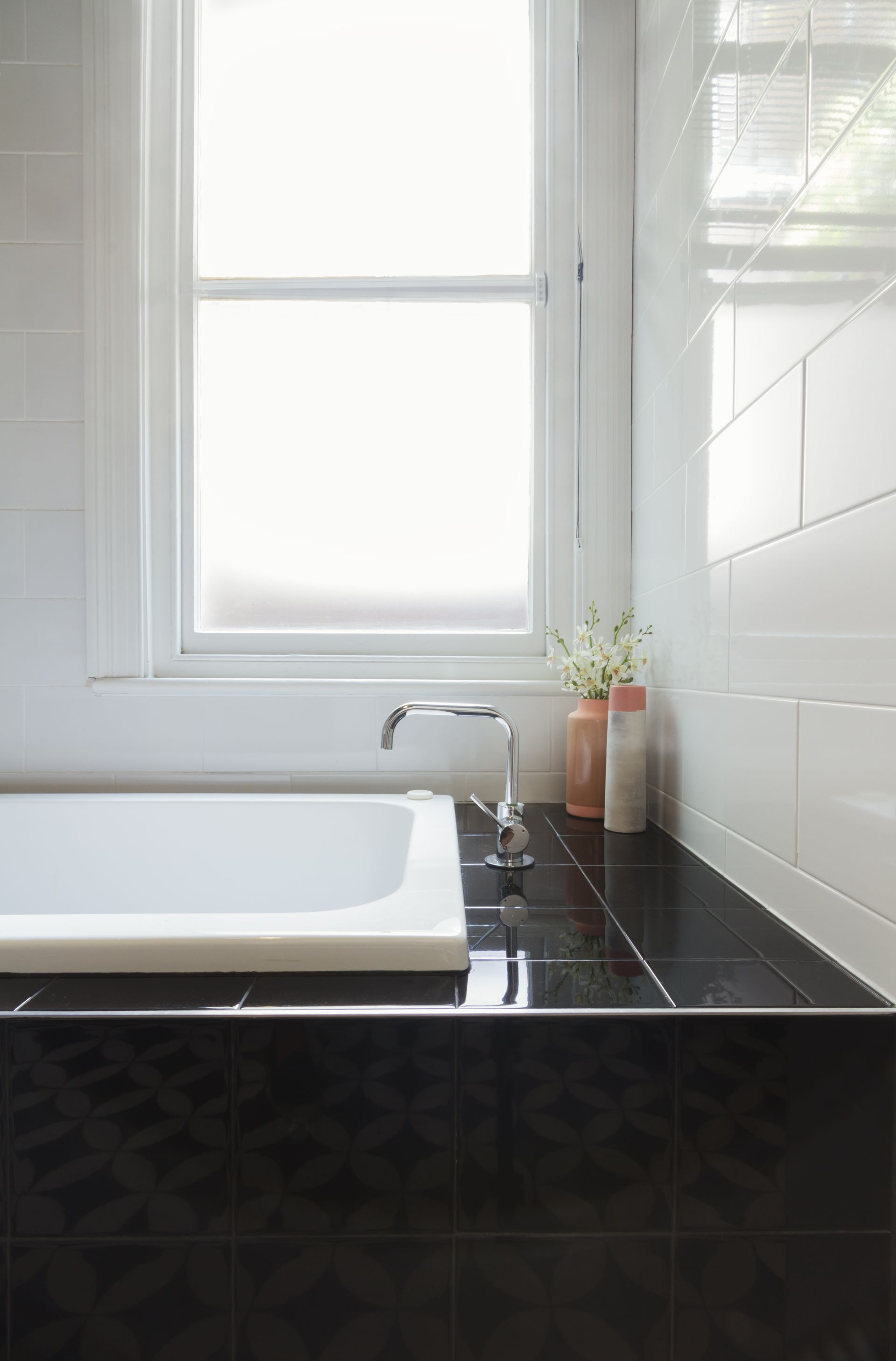 Bathtub by a window, black tile surround, white and black tiles, minimalist design.