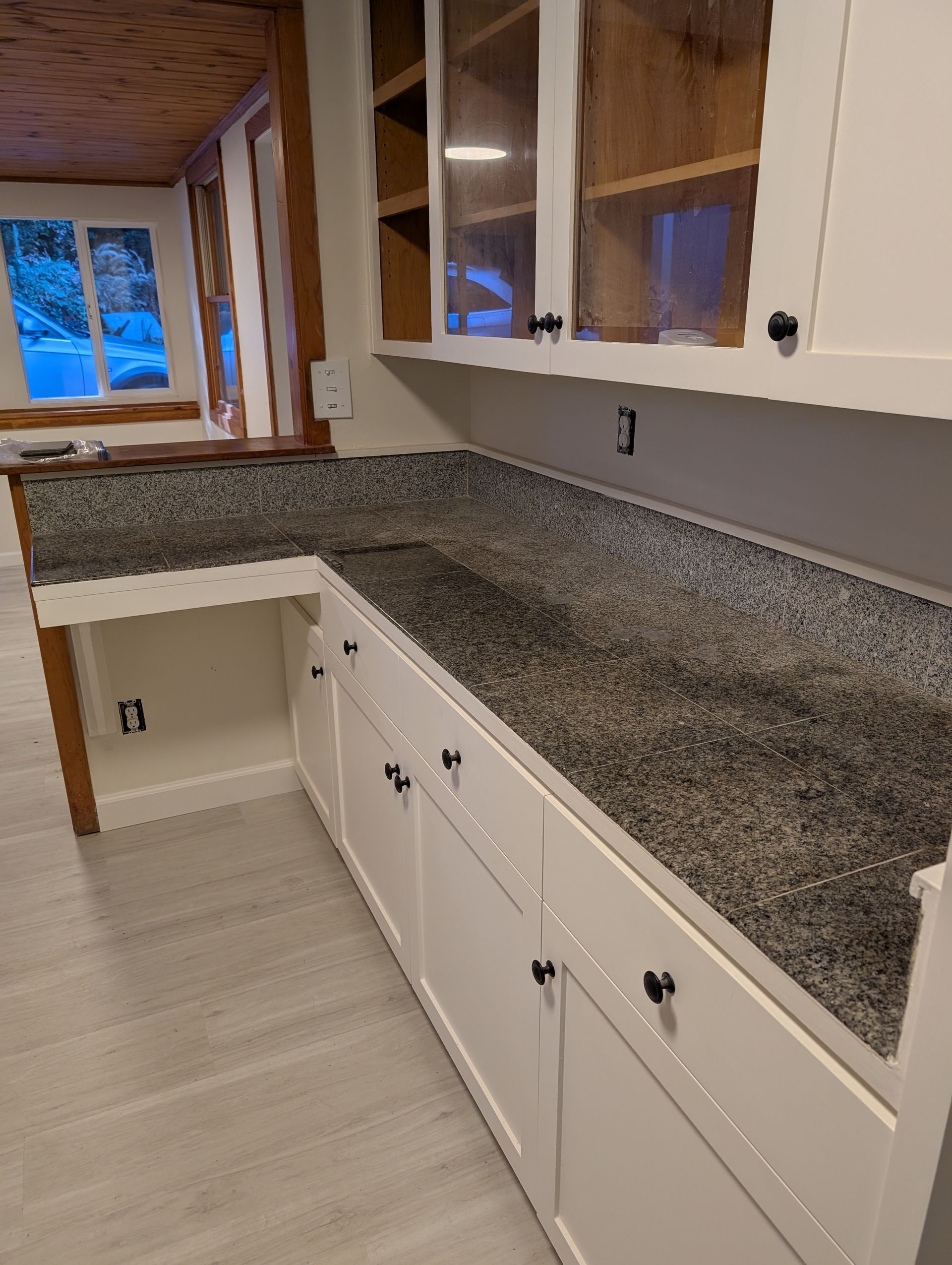 White kitchen cabinets with black speckled countertops and upper cabinets.