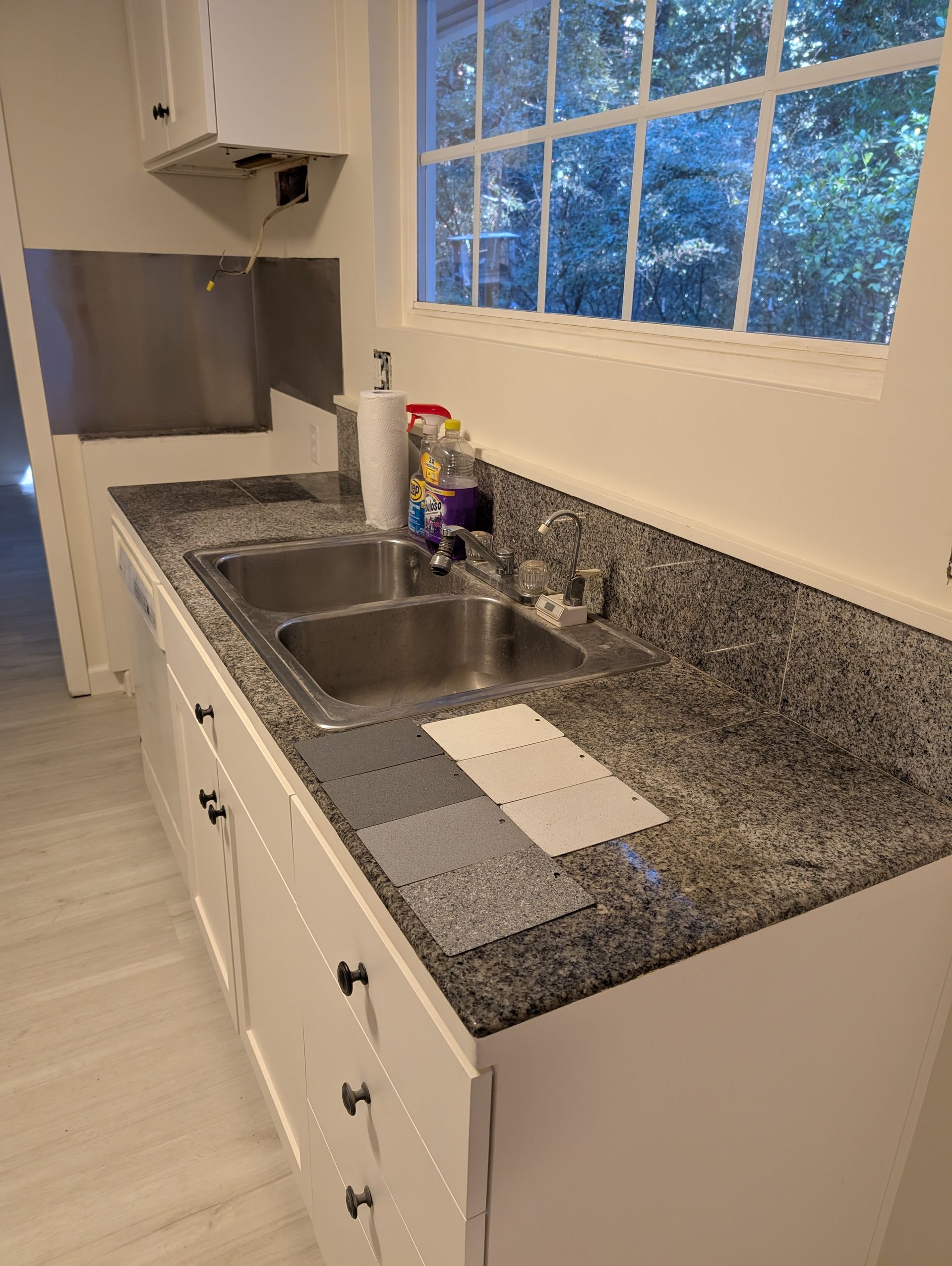 Modern kitchen with light wood cabinets, white countertops, stainless steel range hood.