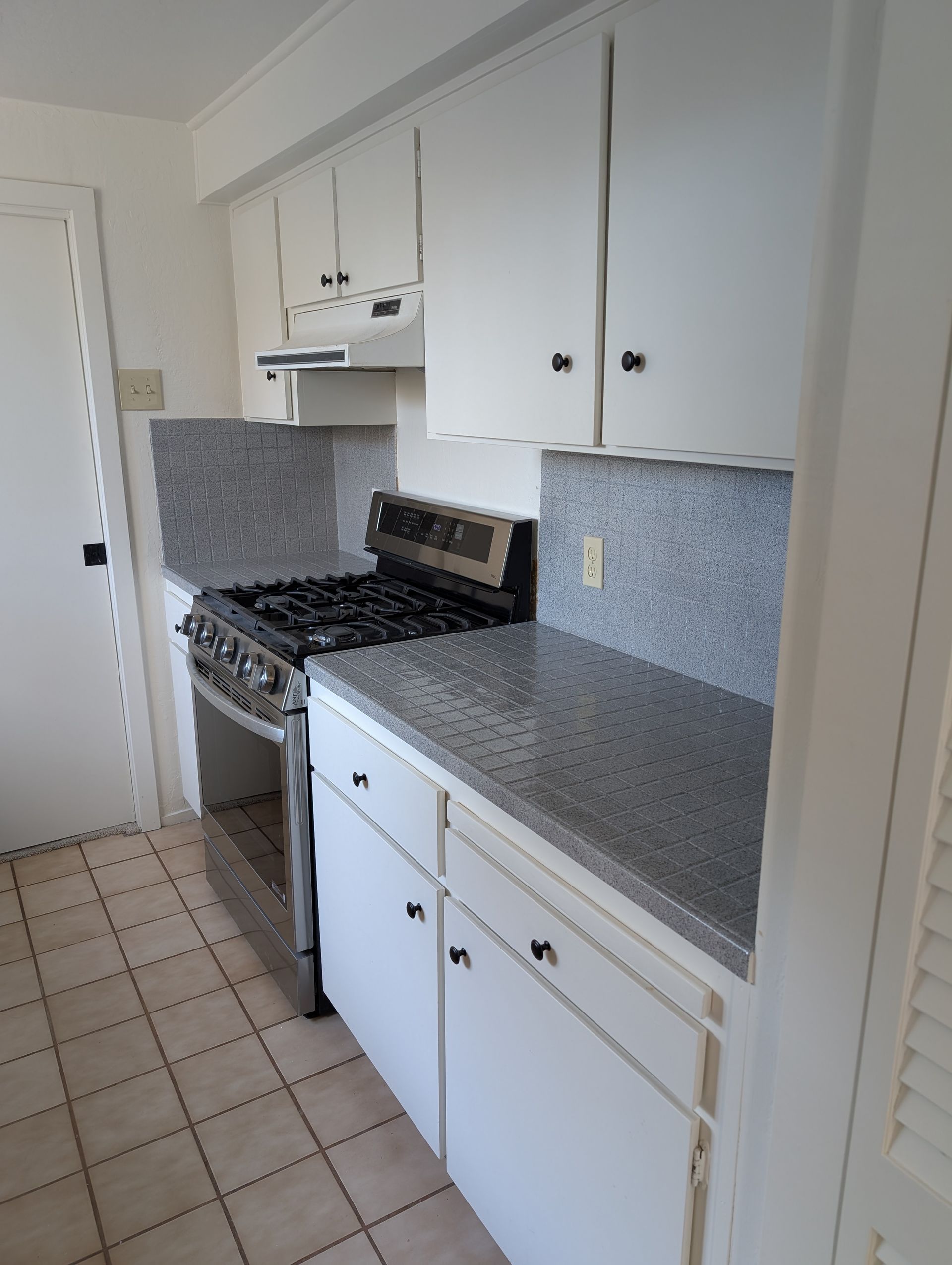 Kitchen with white cabinets, stainless steel stove, and grey countertops and backsplash.