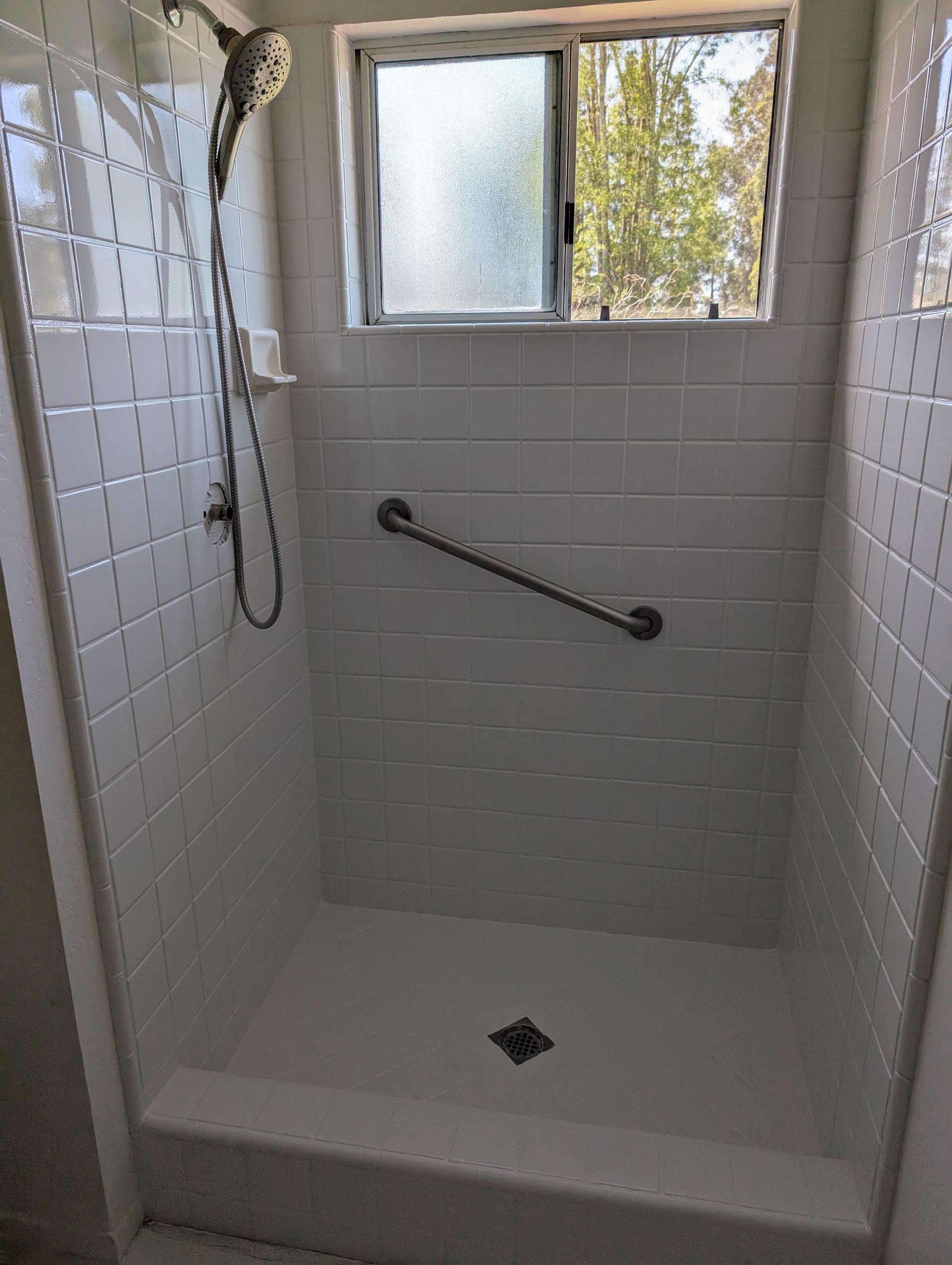 White tiled shower with a grab bar and window.