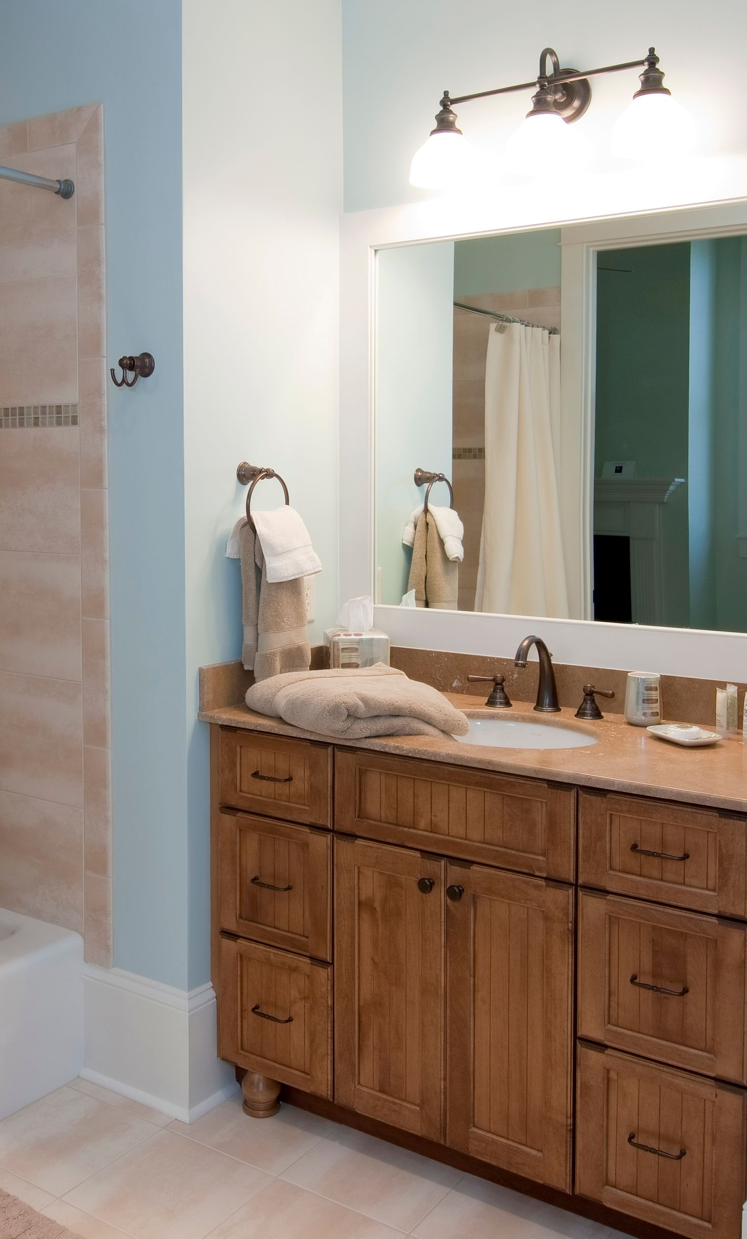 Spacious bathroom with glass shower, marble walls, and a chandelier. A standalone tub is in the background.