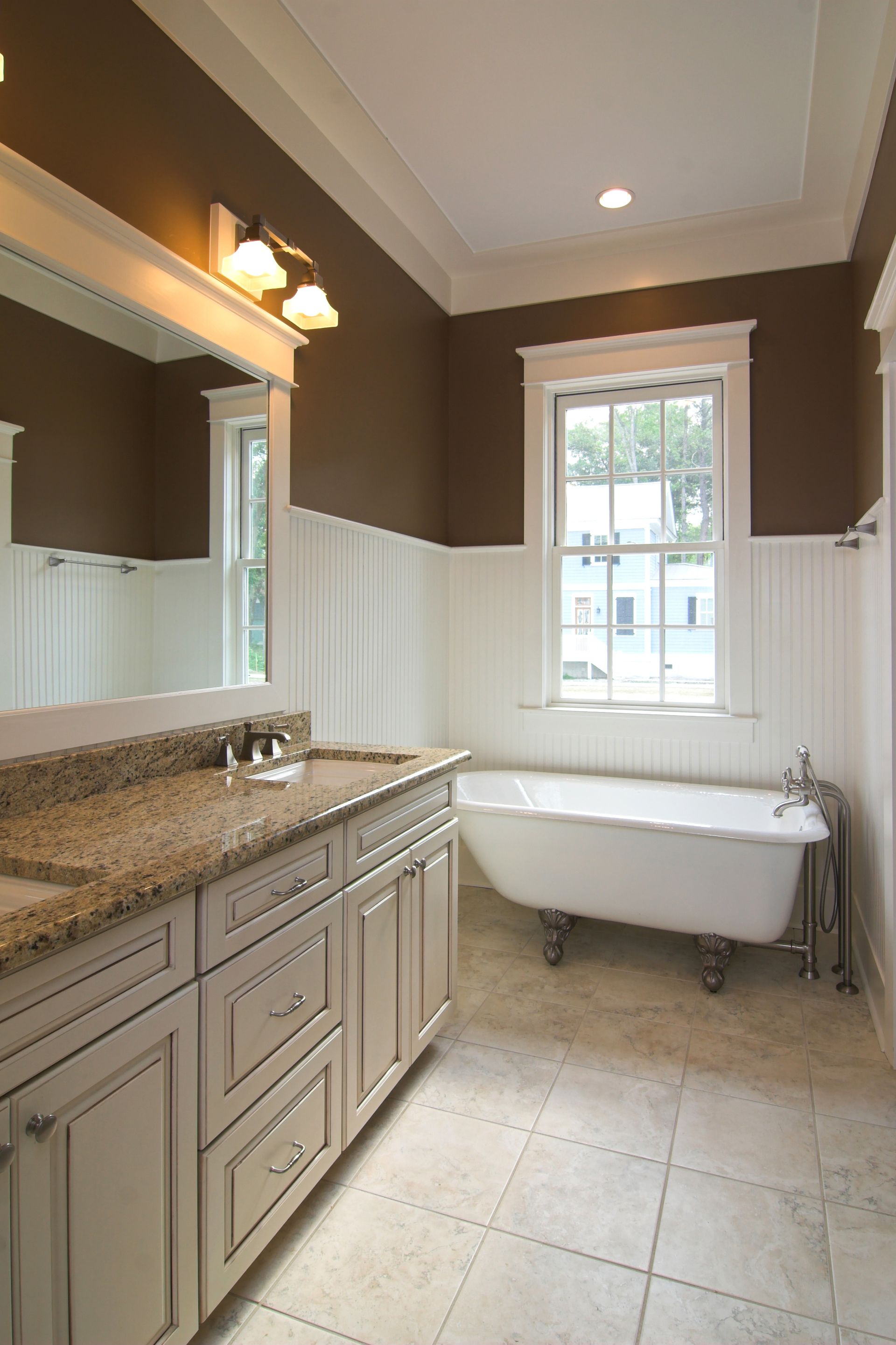 Bathroom with white wainscoting, brown walls, a soaking tub, and a vanity with a granite countertop.