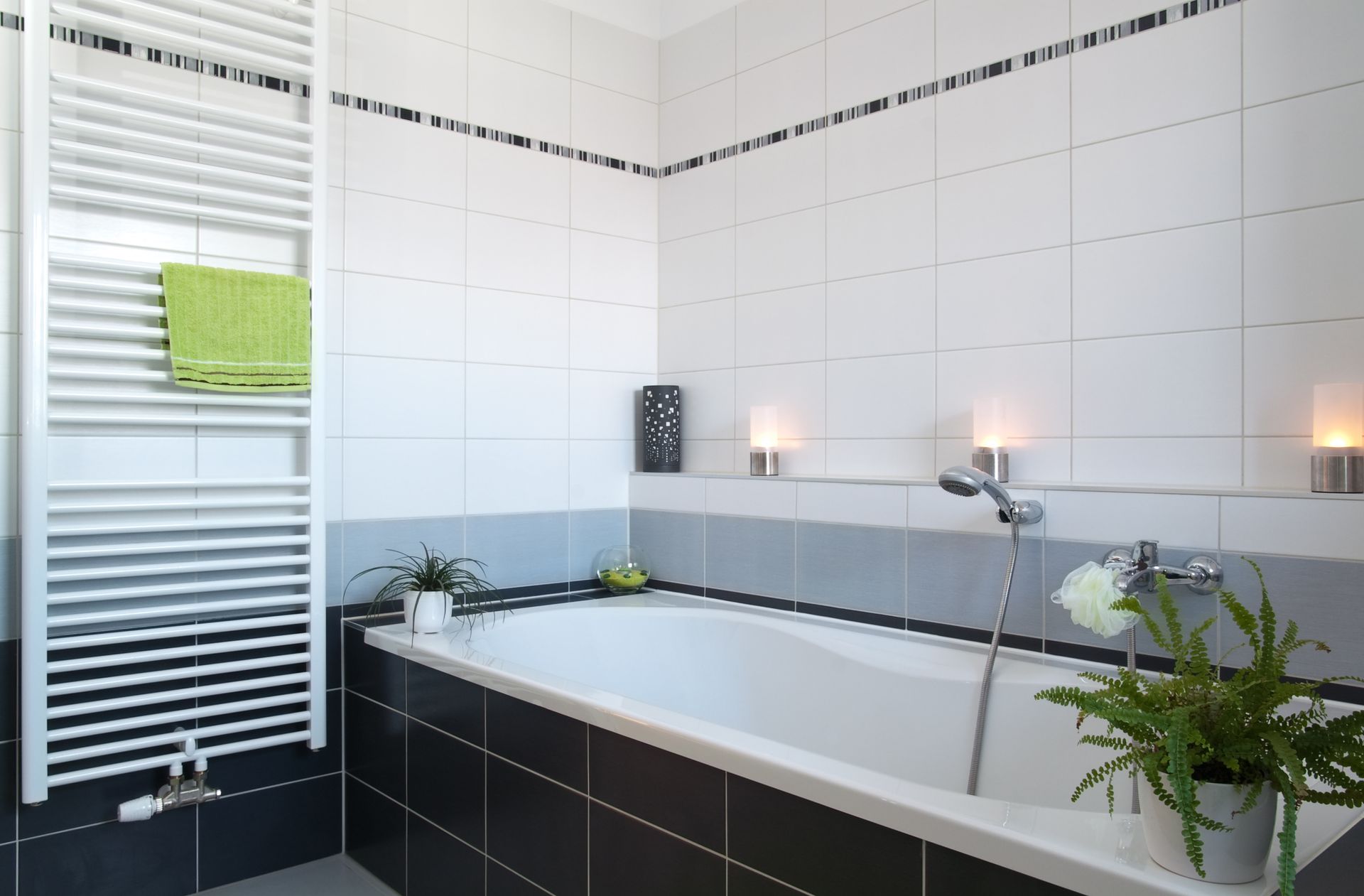 White bathroom with a bathtub, tiles, radiator, and a green towel.
