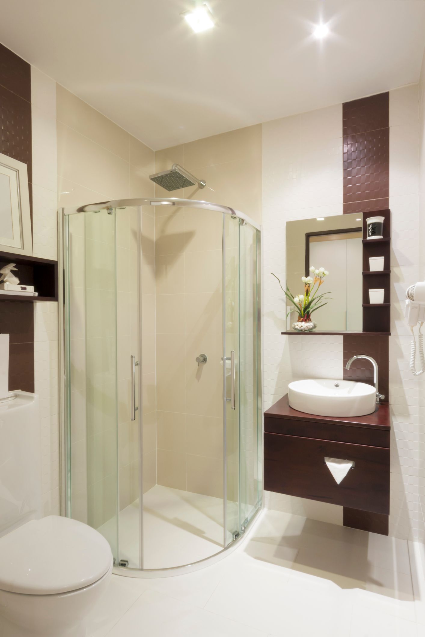 Modern bathroom with a curved glass shower, toilet, and dark wood vanity.