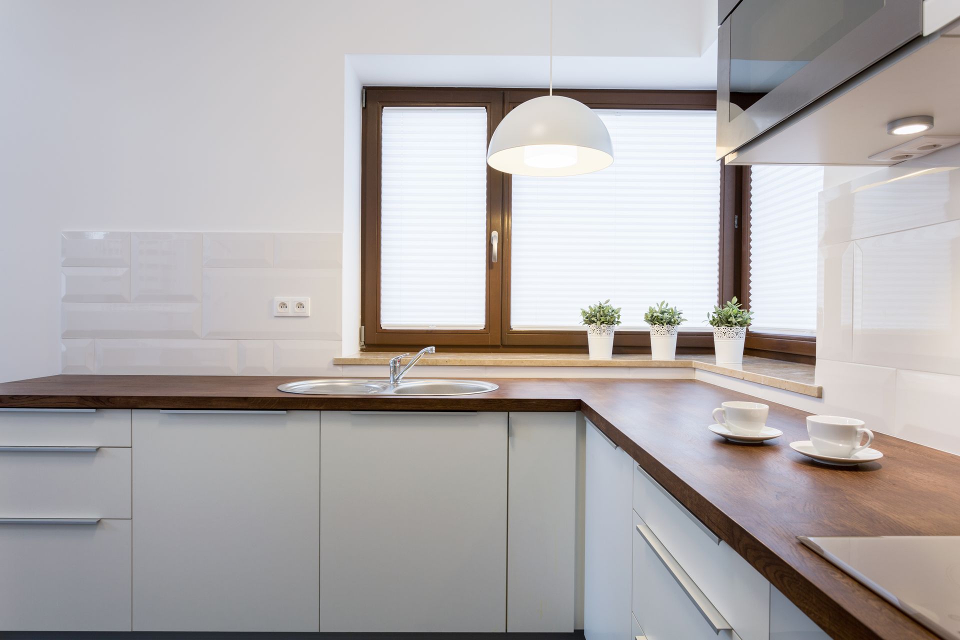 Modern kitchen with white cabinets, wood countertop, and a window with blinds.