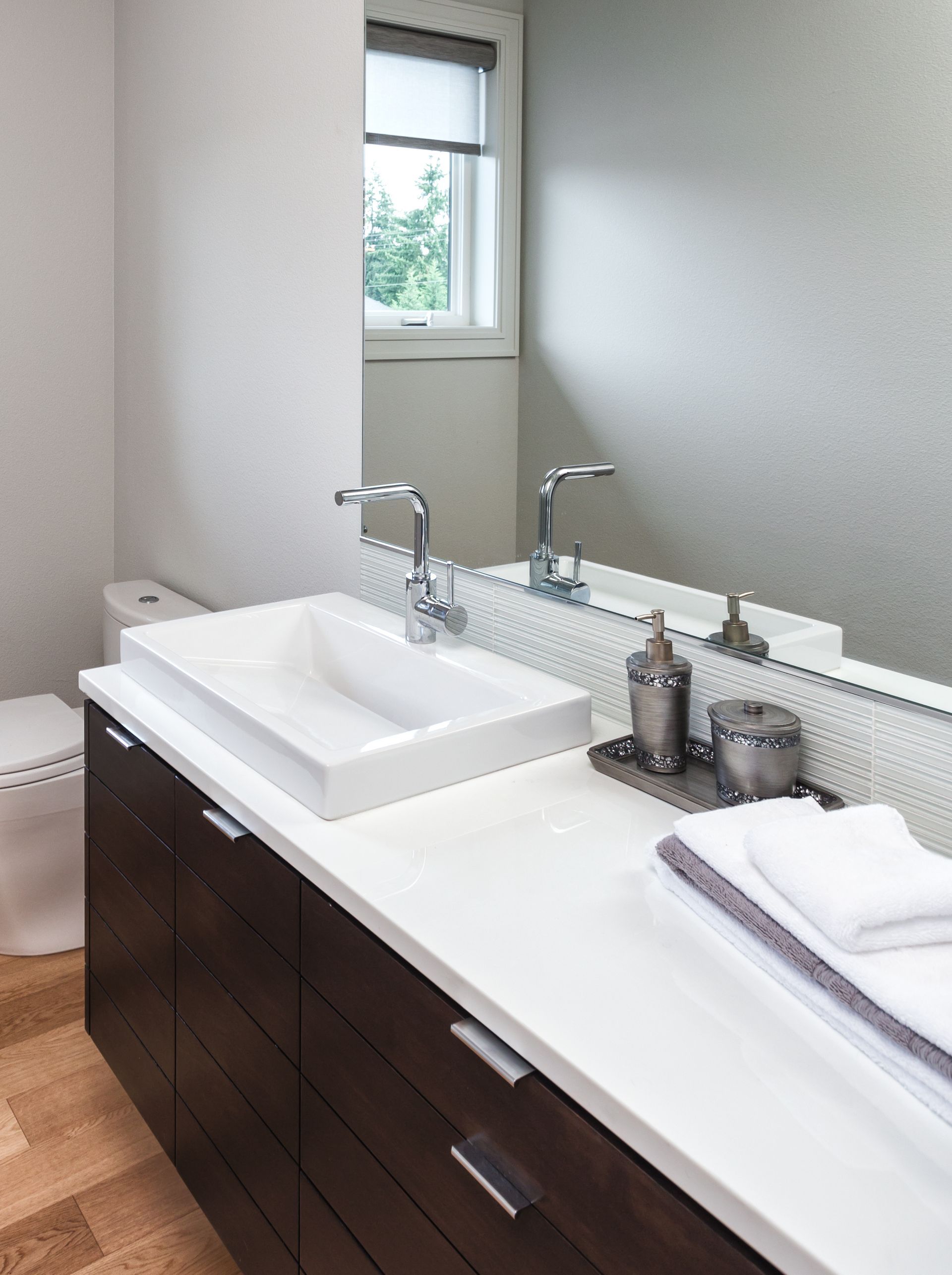 Modern bathroom with a rectangular sink on a dark wood cabinet, white countertop, and large mirror.