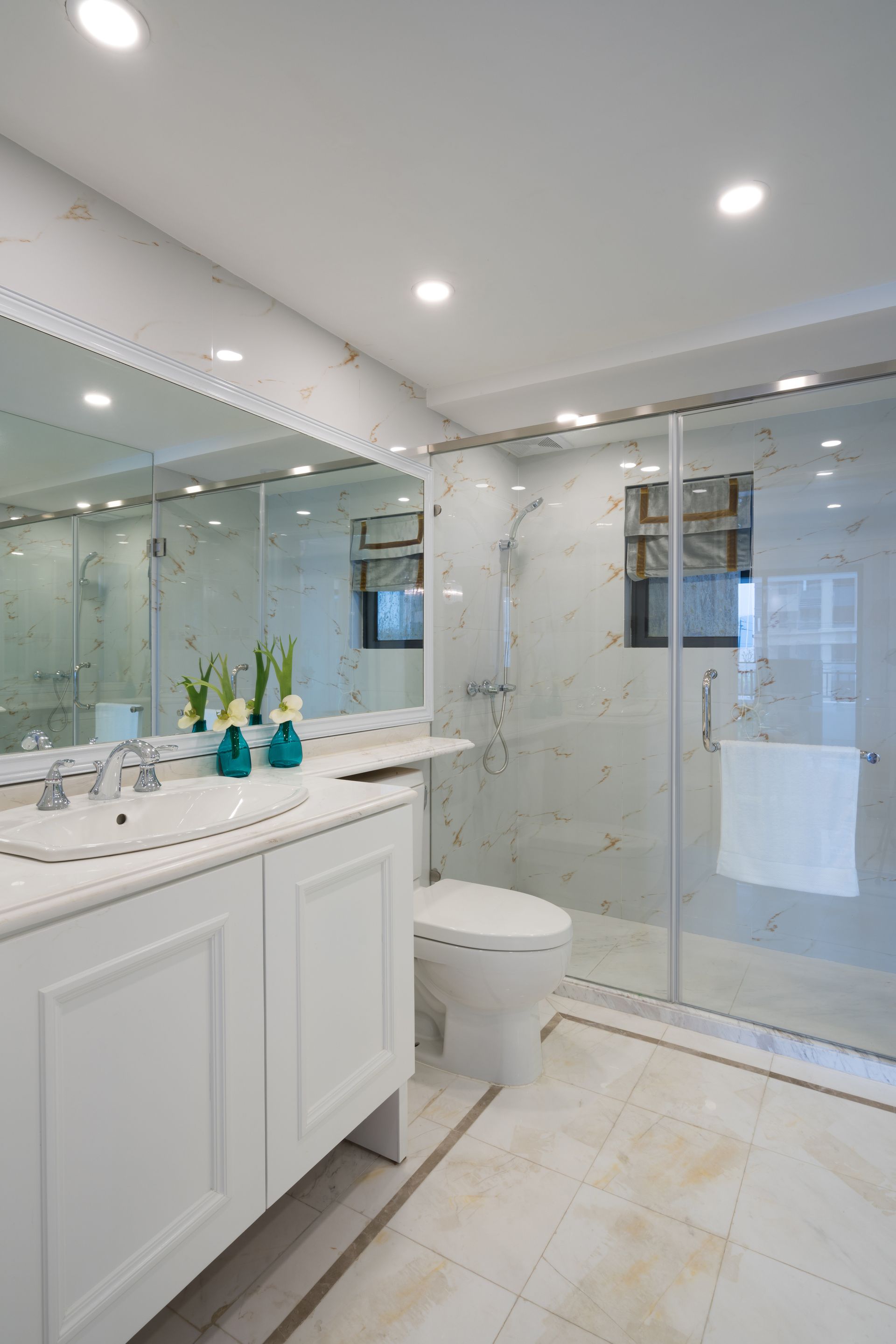 Spacious white bathroom with double sinks, soaking tub, glass shower, and dark wood floor.