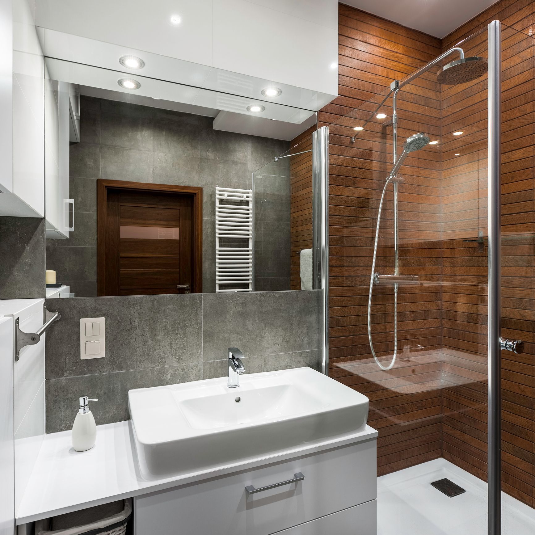 Modern bathroom with white vanity and sink, shower with glass door, and wood paneling.