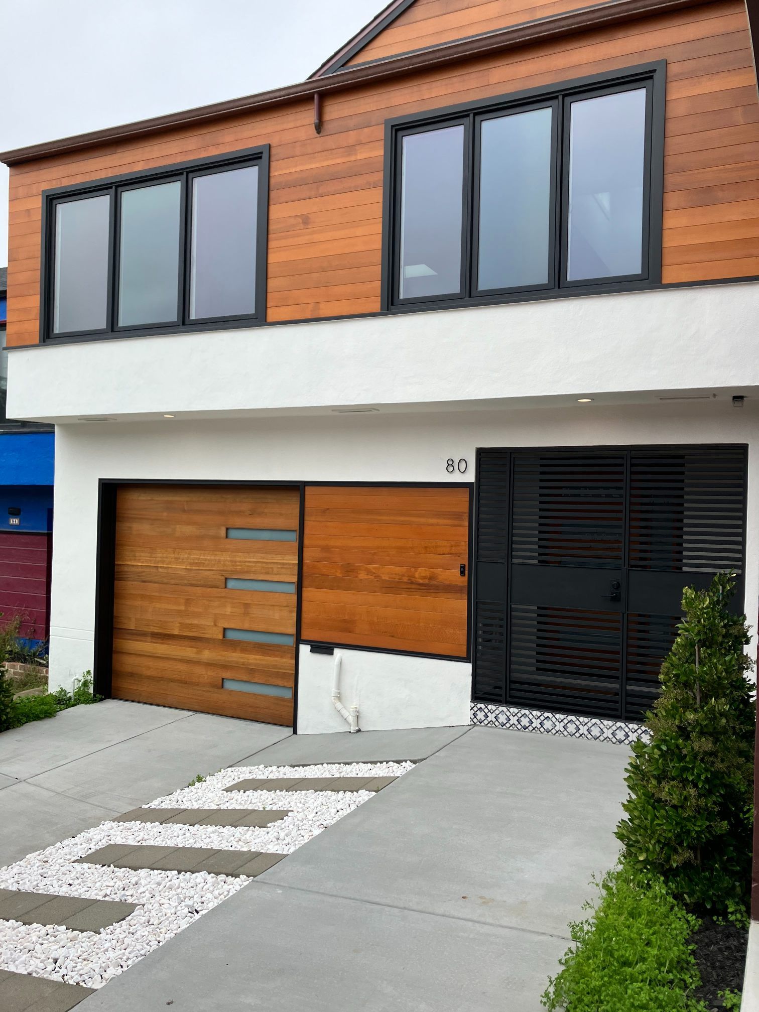 Modern two-story house with wood garage, dark windows, and concrete driveway with painted walkway stripes