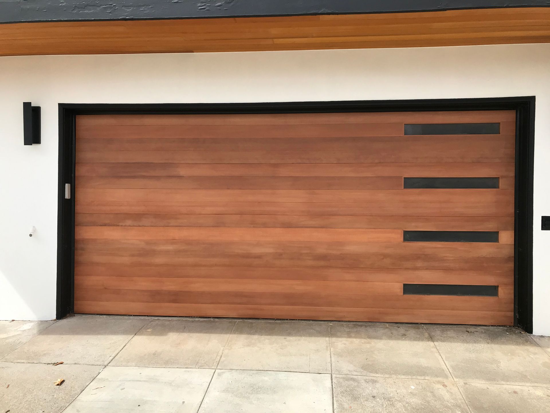 Modern wooden garage door with black trim on a white exterior wall