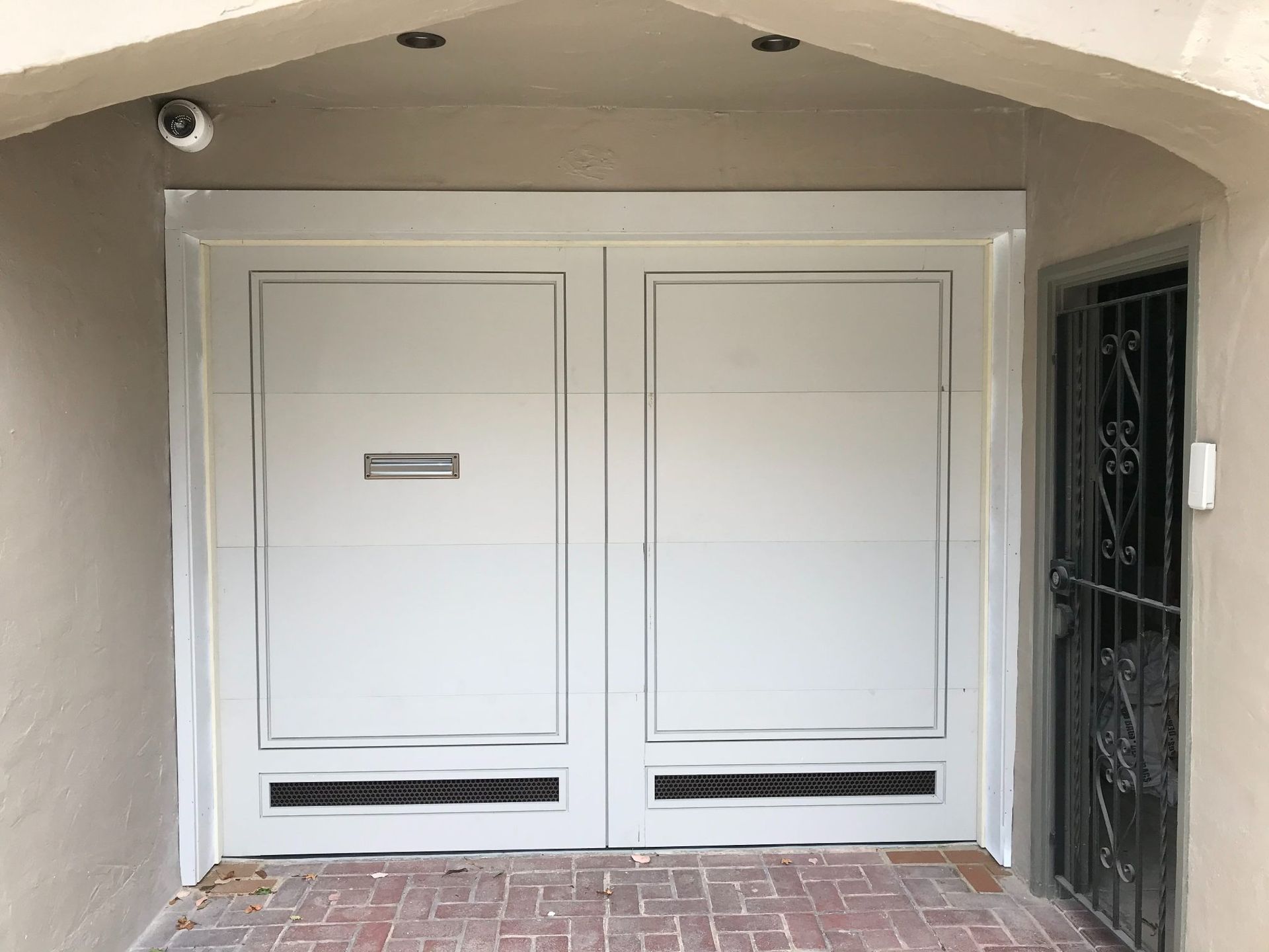 White double front door with small mail slot under a stucco archway, with a side security gate.
