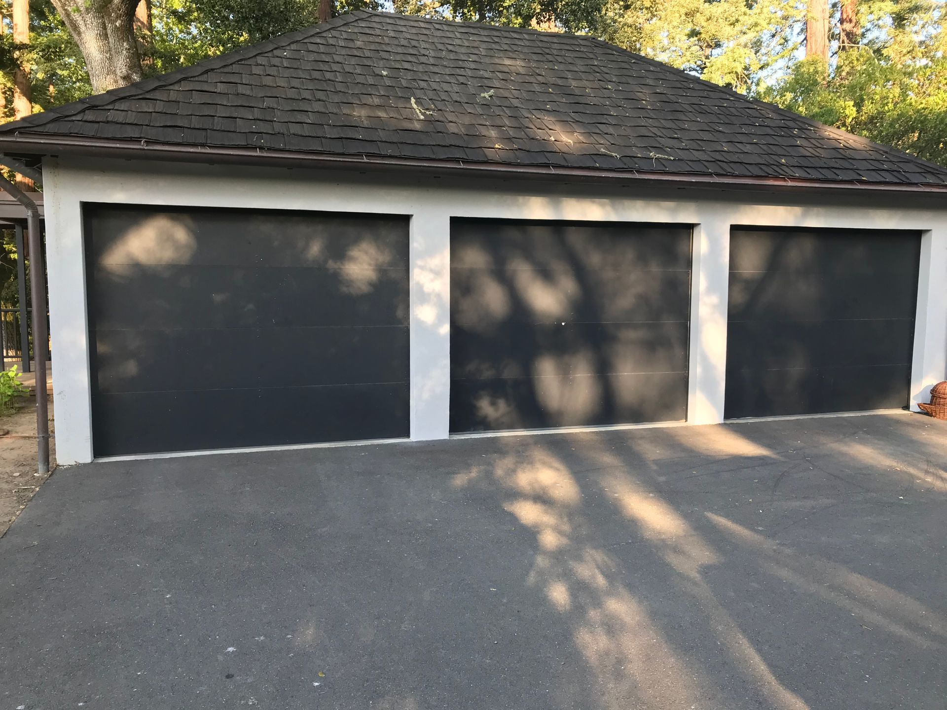 A garage with three black garage doors and a black roof